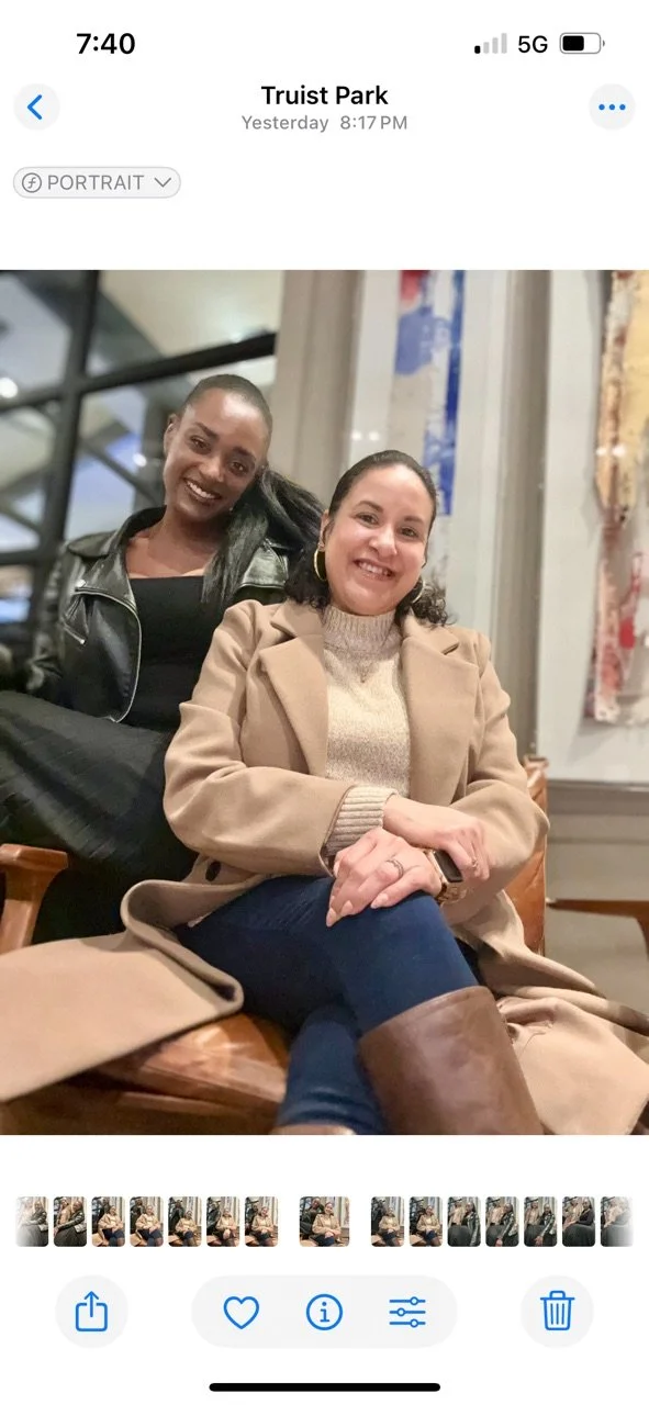 Two women sitting and smiling at Truist Park, one wearing a beige coat and the other in a black leather jacket.