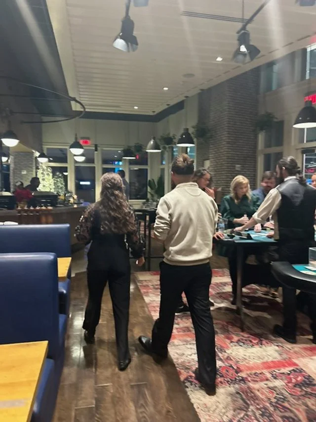 People socializing and chatting in a modern restaurant or bar with high ceilings, hanging lights, and a brick wall.