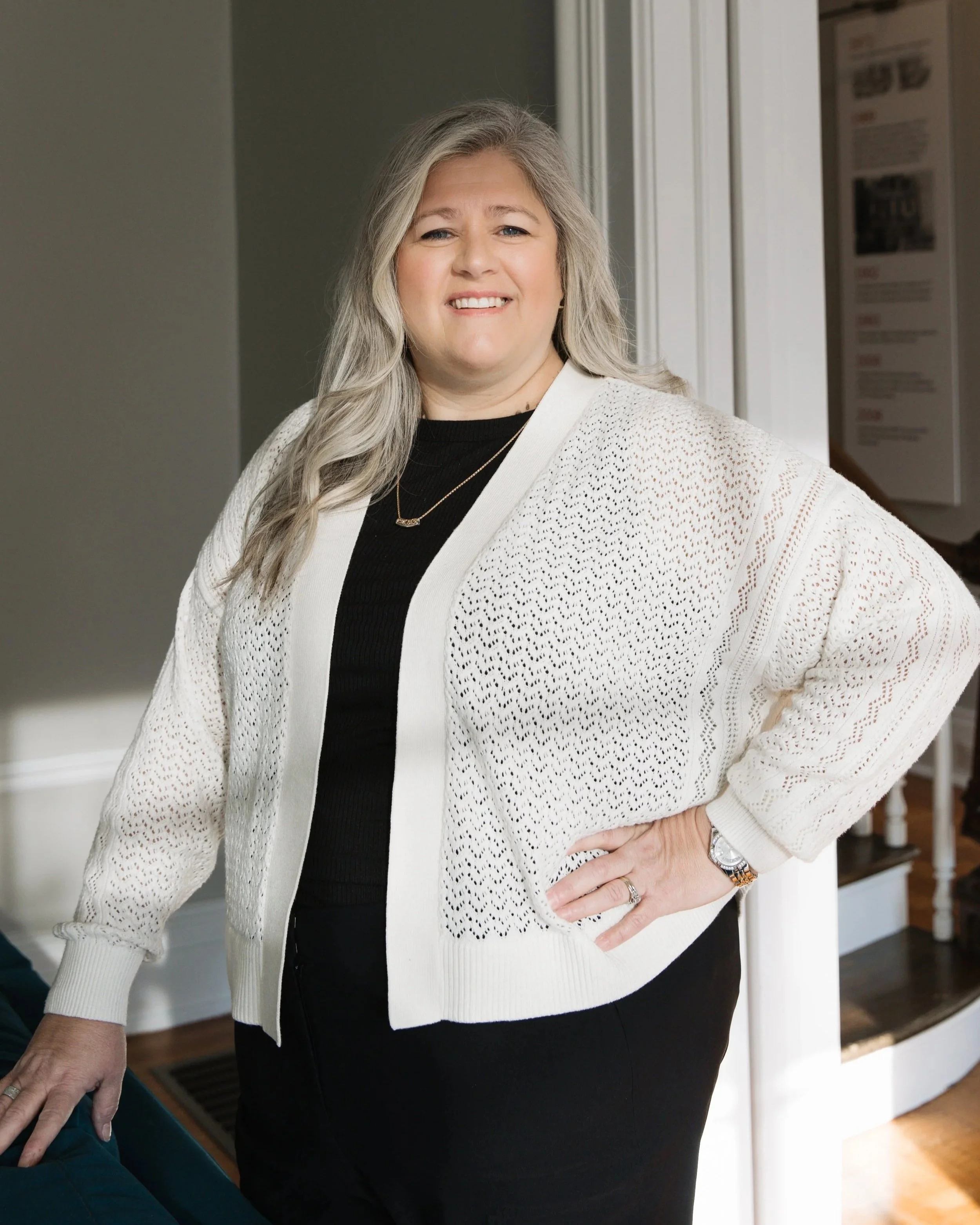 A young woman with dark, wavy hair in a red long-sleeve top smiling widely with teeth showing.