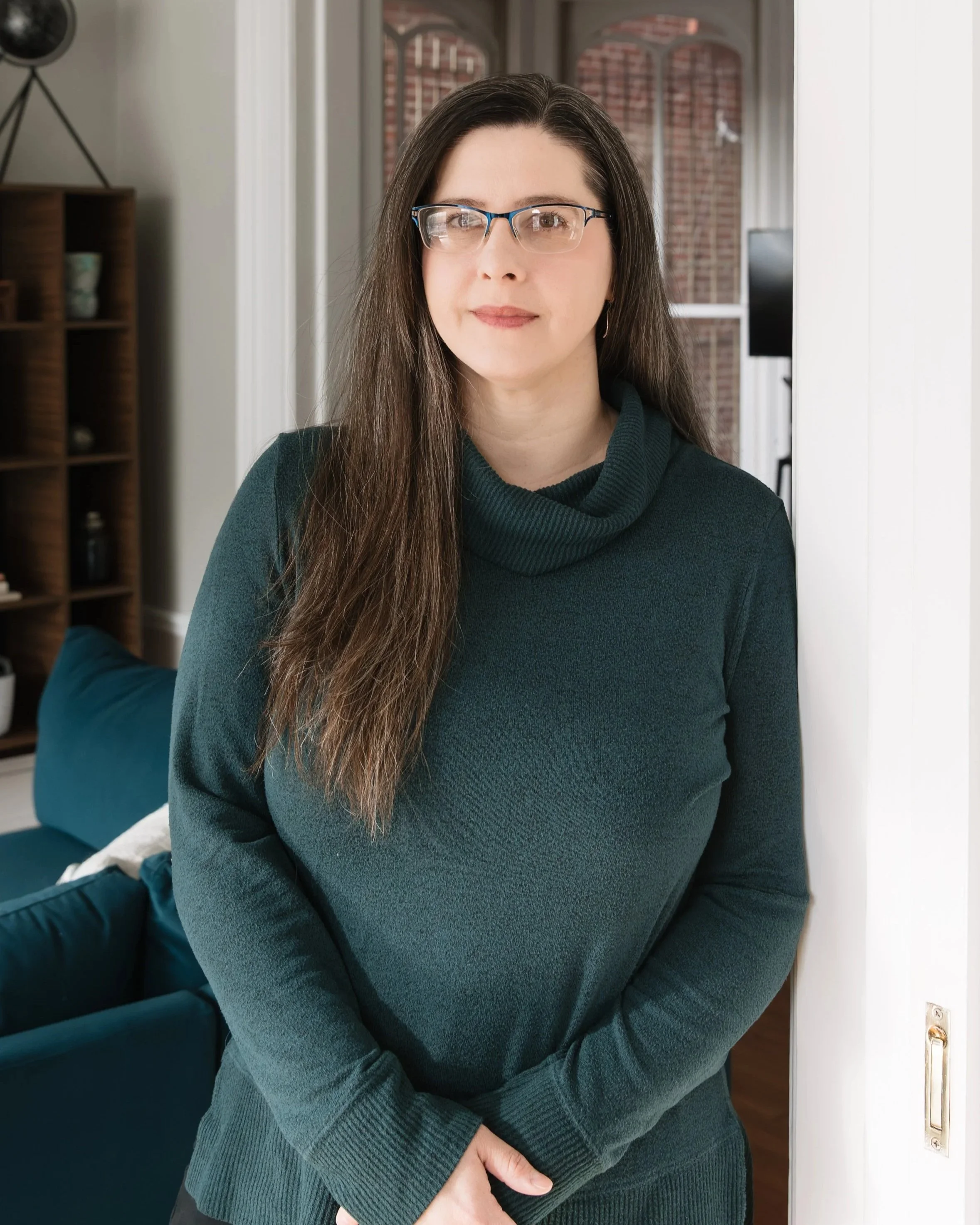 A man with a beard and short dark hair standing on a beach with boats in the background.