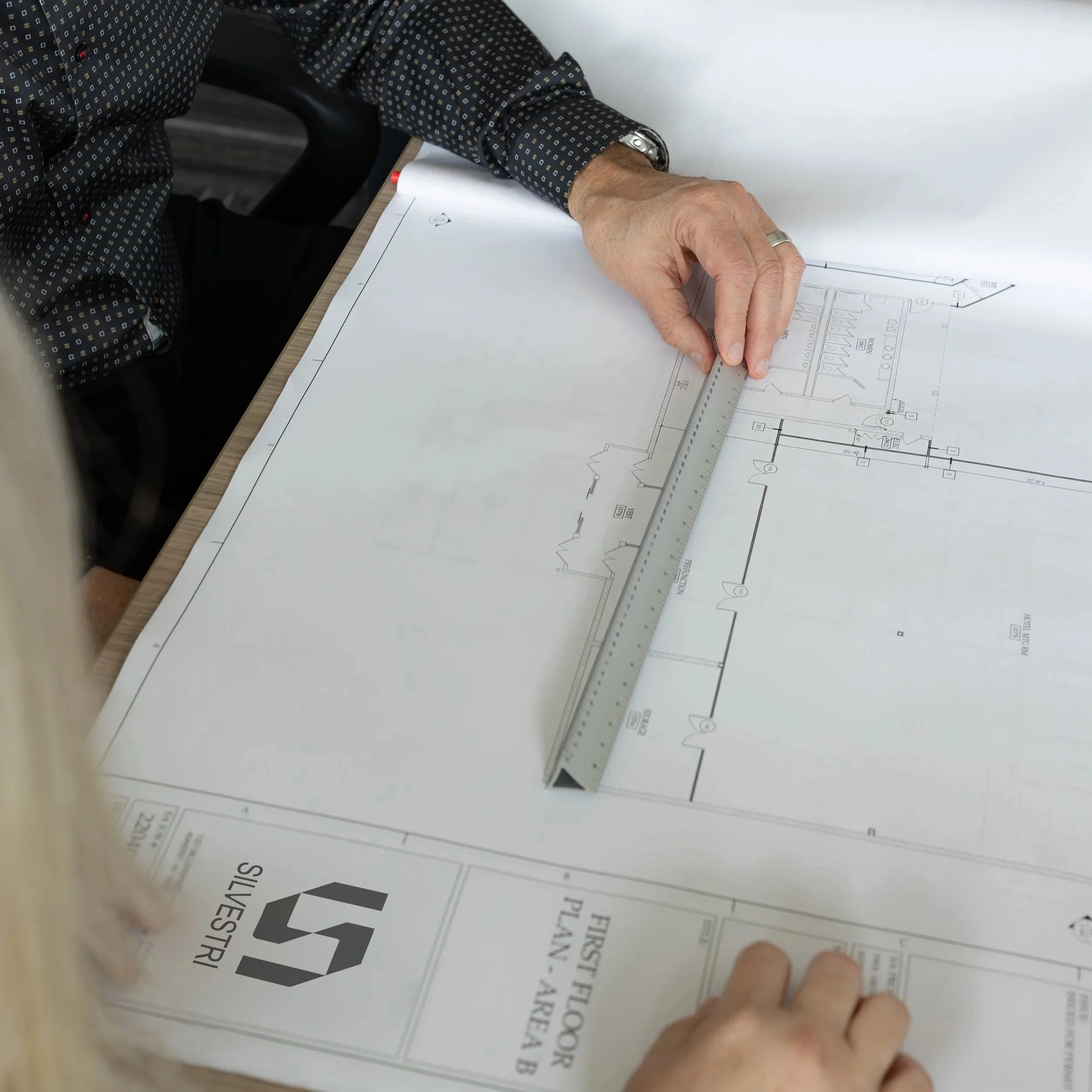 Person using a ruler to measure a blueprint for a building or construction project on a large table.