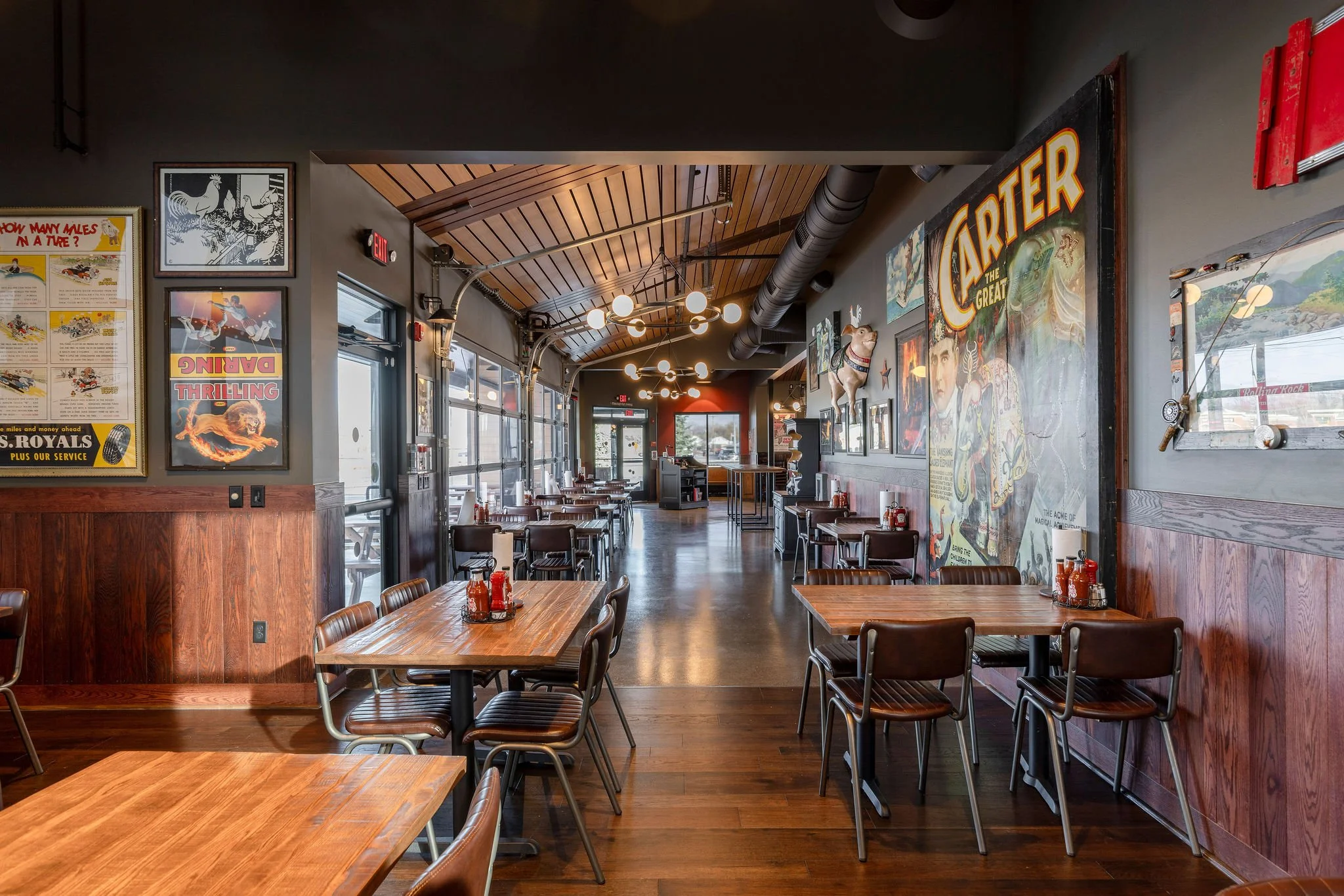 Interior of a vintage-style restaurant with wooden tables and chairs, decorative posters on the walls, and large windows allowing natural light inside.