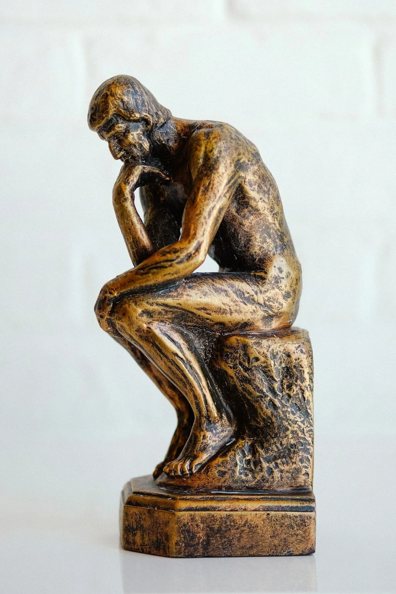 A bronze sculpture of a man sitting on a block, with his chin resting on his hand, in a pondering pose.