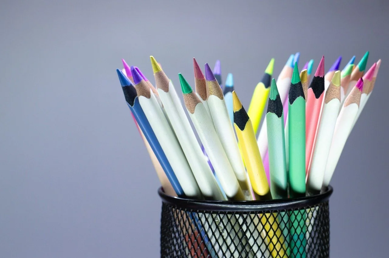 A black mesh pen holder filled with colorful colored pencils.