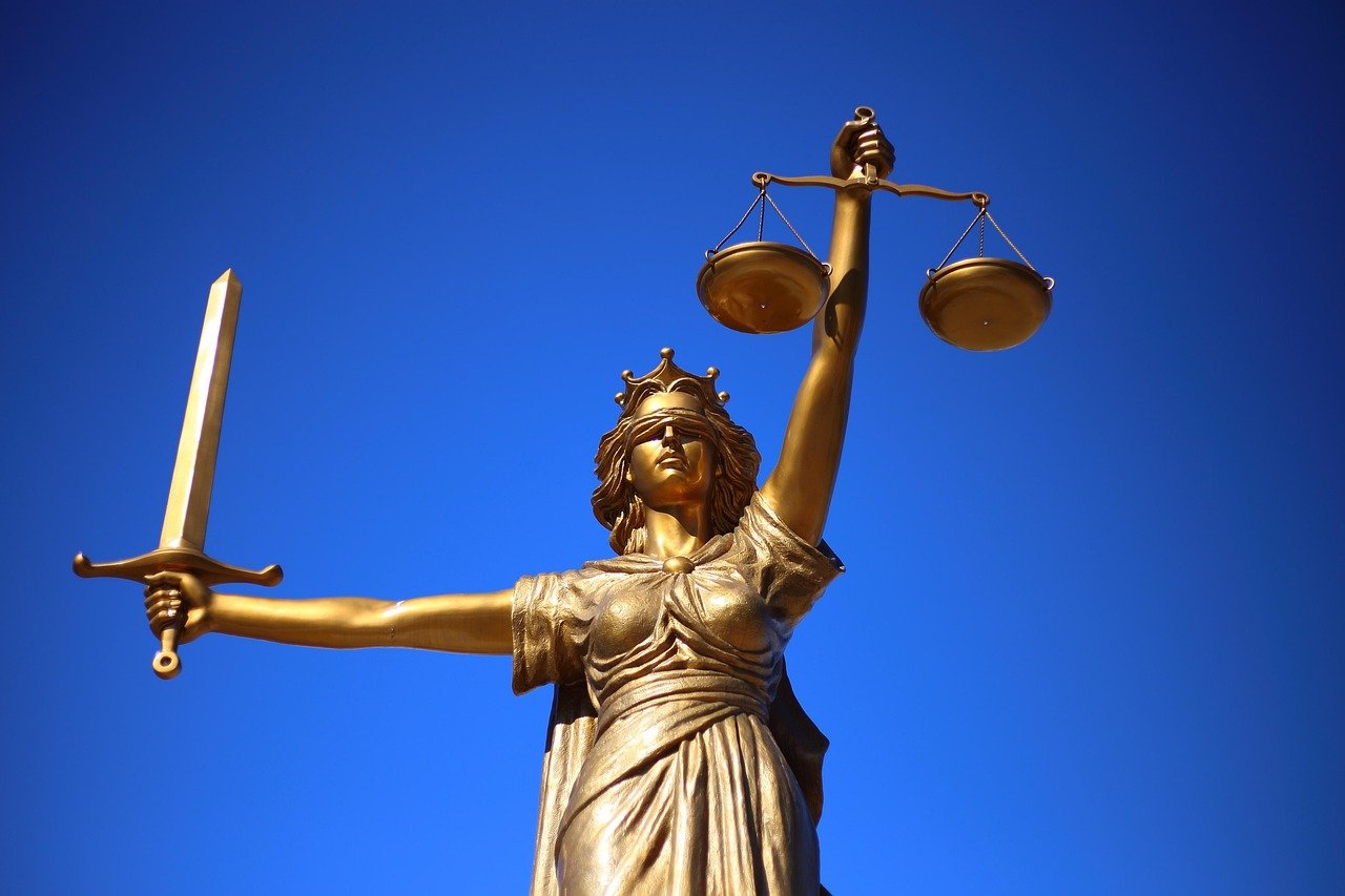 Gold statue of Lady Justice holding a sword in her right hand and scales in her left hand, set against a clear blue sky.