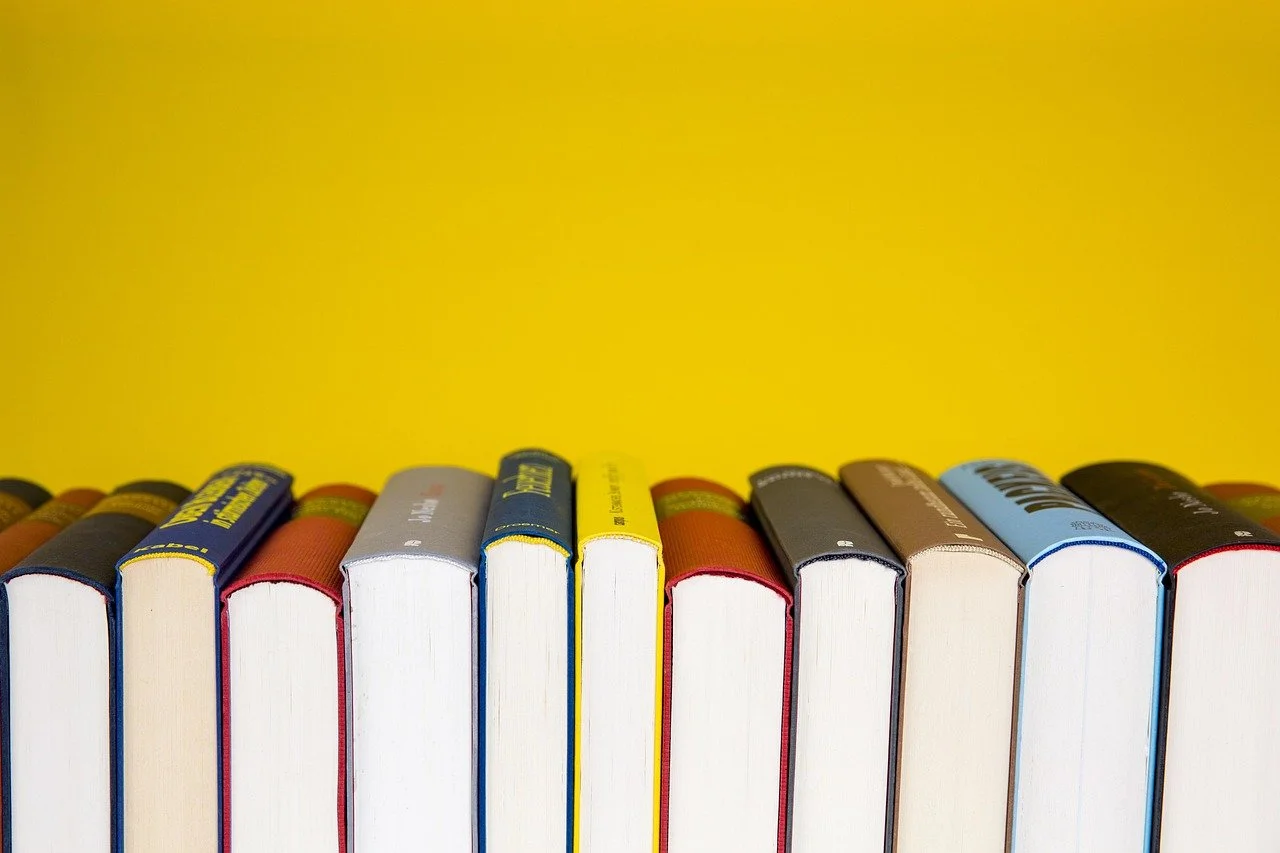 A row of colorful books with their spines facing backward against a yellow background.