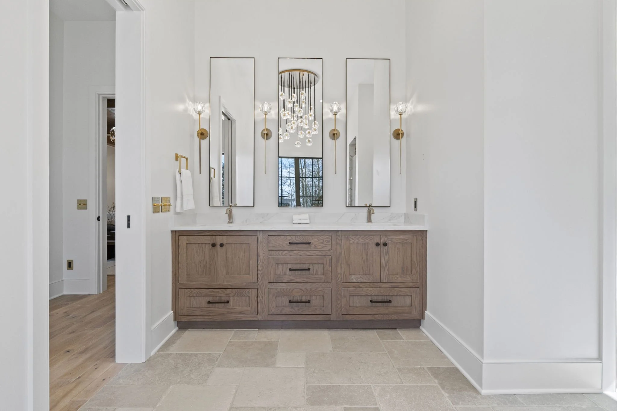 Modern bathroom vanity with two sinks, three mirrors, and decorative wall sconces.
