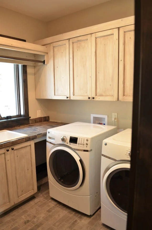 A laundry room with wooden cabinets, a window, a countertop, a white washing machine, and a white dryer.