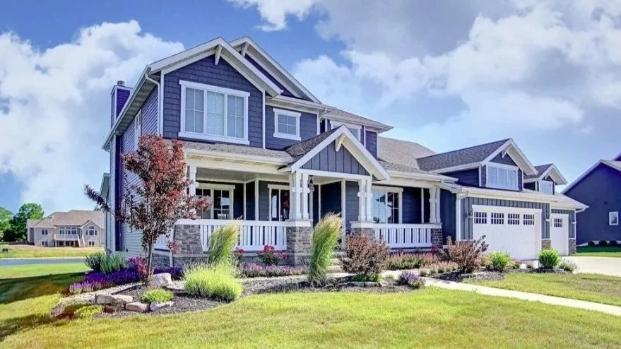 A modern two-story house with a blue exterior, white trim, front porch, attached garage, and landscaped yard.