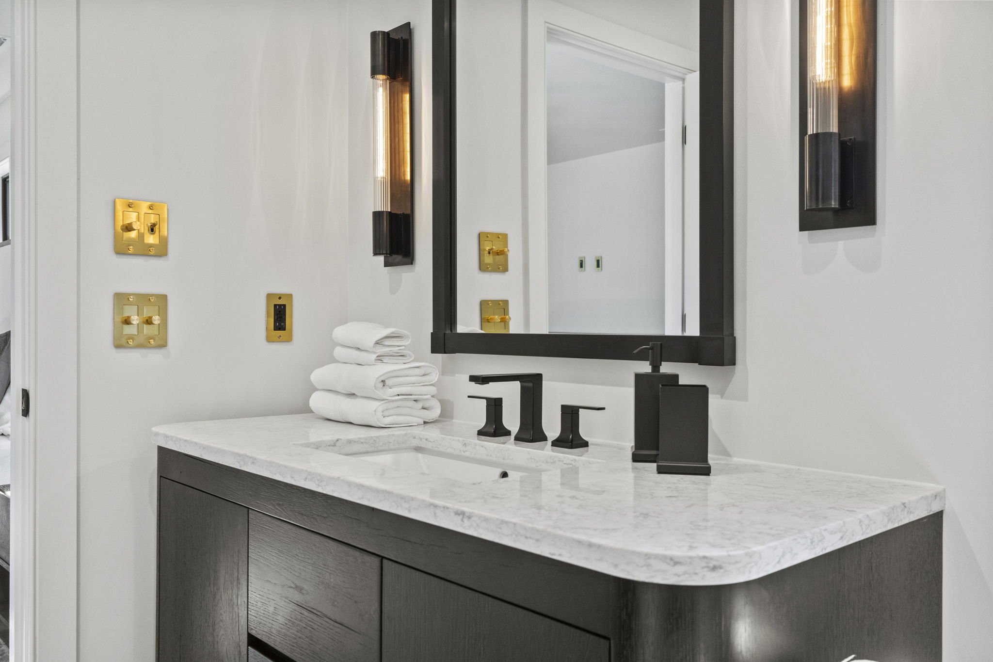 Modern bathroom vanity with black fixtures, white marble countertop, stack of white towels, and a large mirror framed in black.