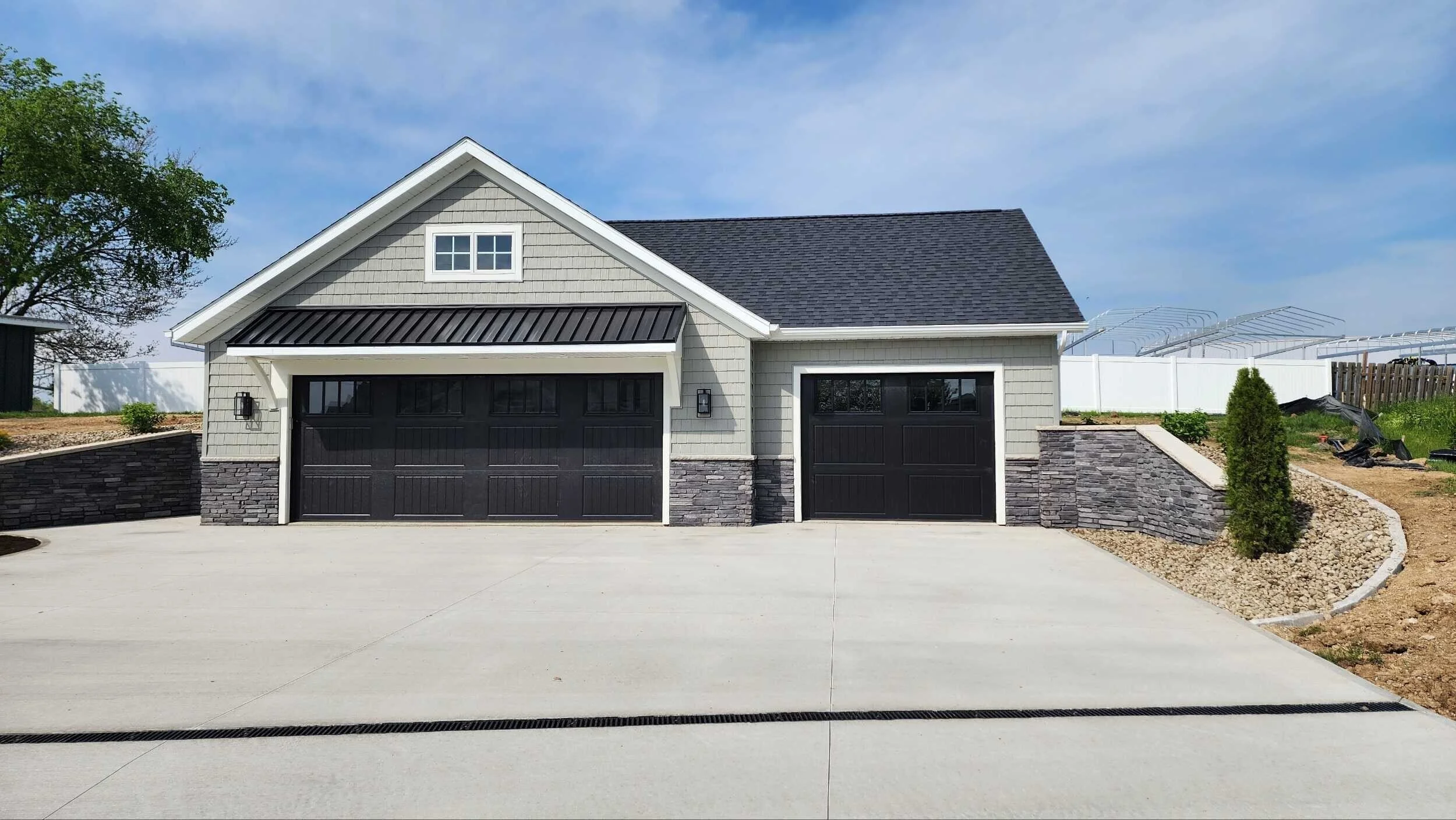 Modern house with a black garage door, gray siding, stone accents, and a sloped roof, with a driveway and landscaping.