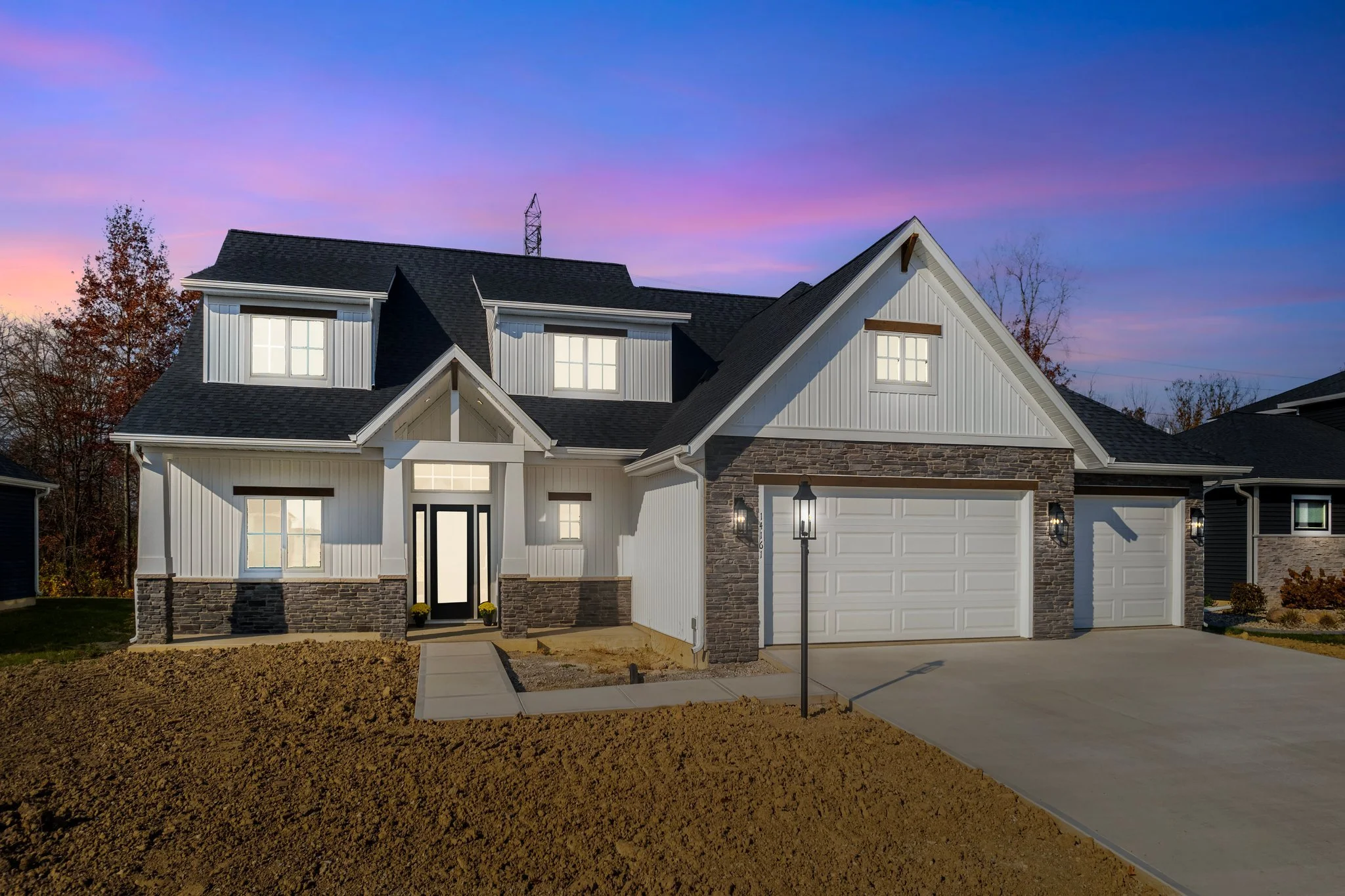 Modern two-story house with white siding and a black roof at dusk, with a three-car garage and front yard under construction.