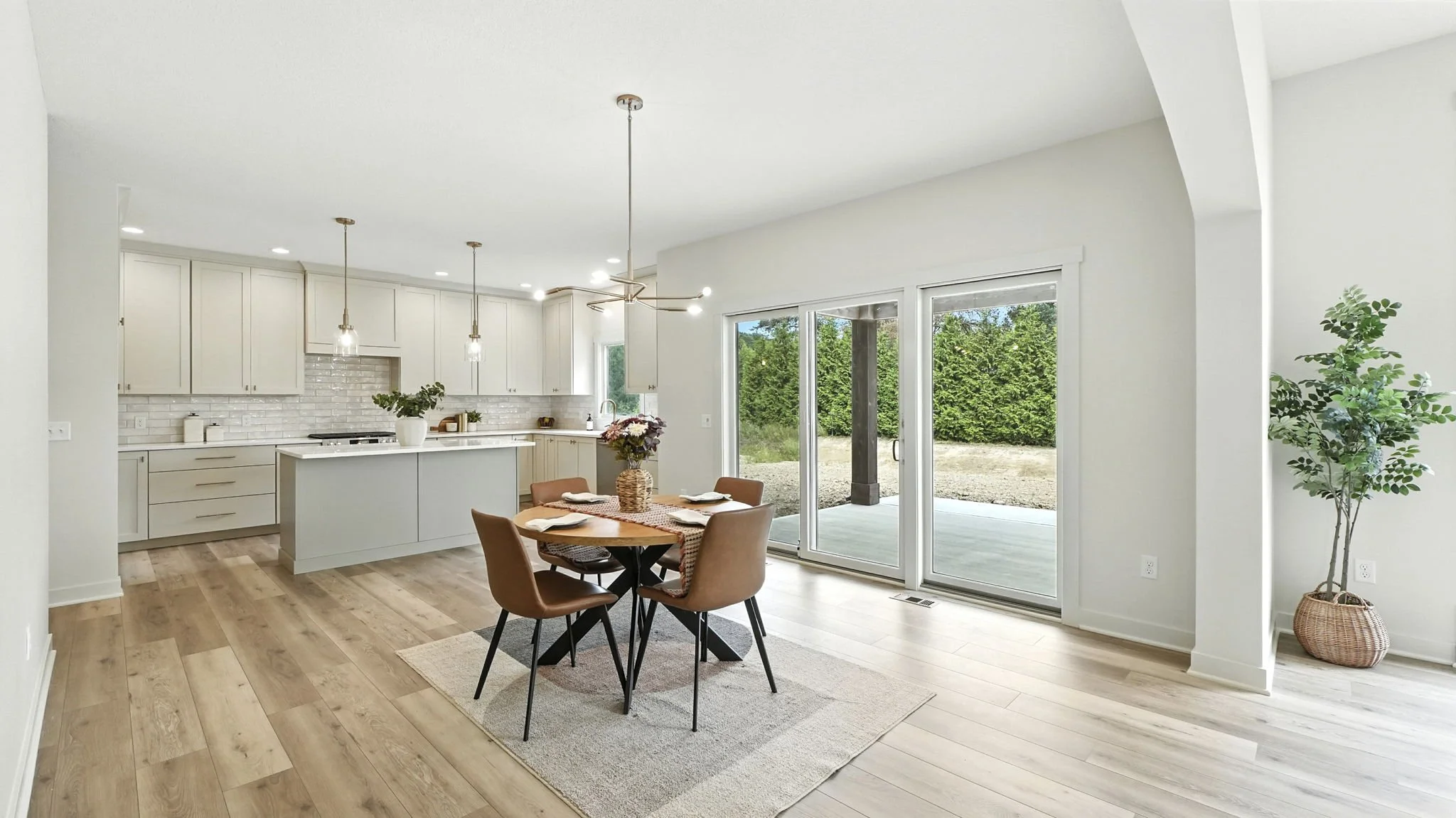 Modern open-concept kitchen and dining area with sliding glass door to backyard, light-colored cabinetry, wooden flooring, and minimalist decor.