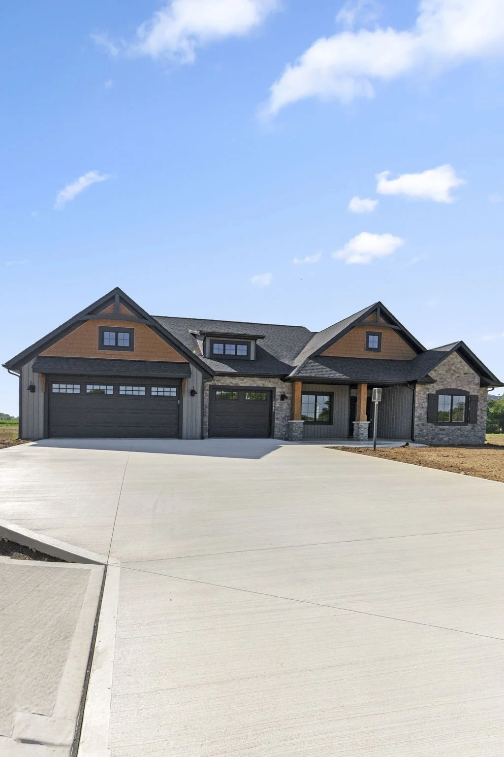 Modern house with a large driveway and landscaped front yard under a blue sky with clouds.