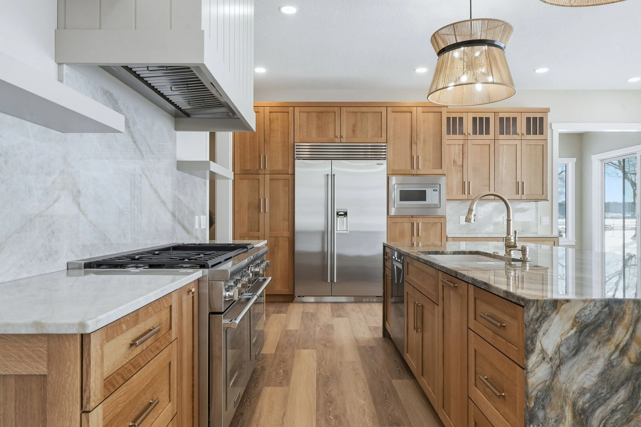 Modern kitchen with wooden cabinets, stainless steel appliances, granite countertops, and a large window letting in natural light.