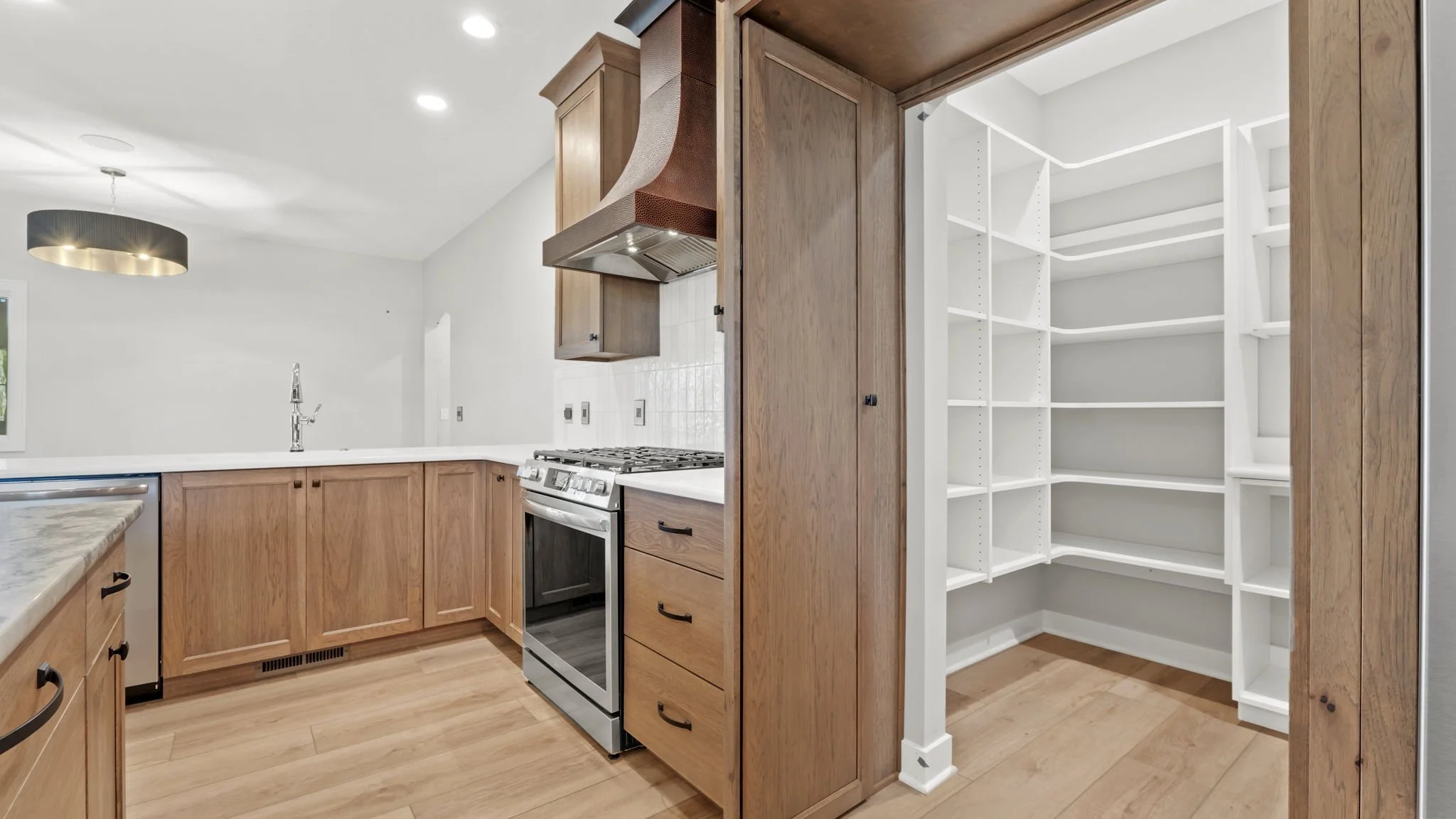 Kitchen with wooden cabinets, stainless steel oven, and an empty walk-in pantry with white shelving.