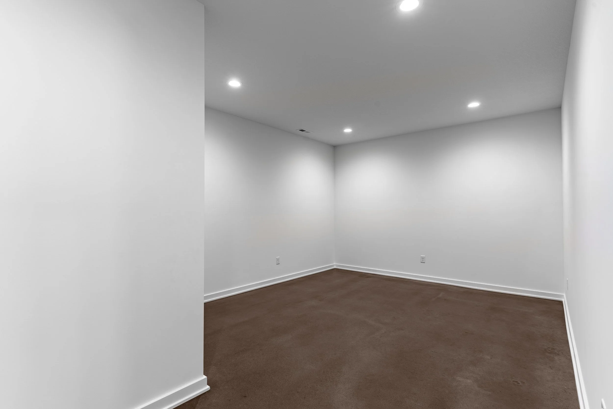 Empty room with white walls, brown carpet, and ceiling lights.