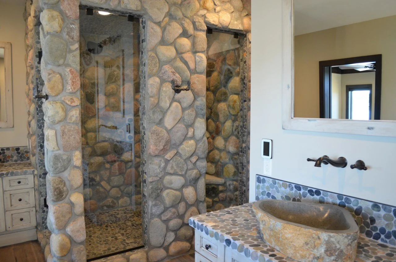 Bathroom with a walk-in shower made of rounded stones, a stone sink on a pebble-tiled vanity, and a mirror.