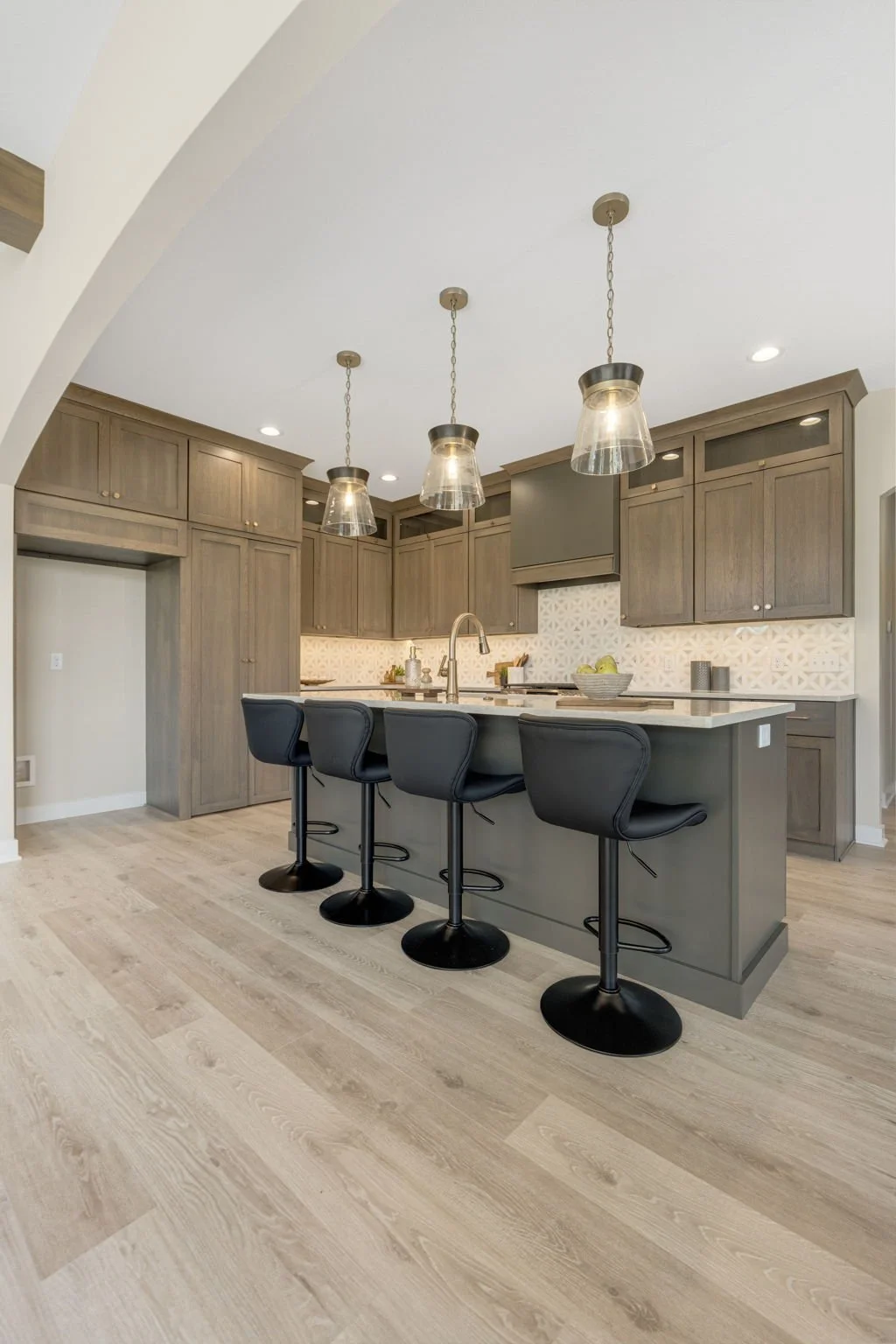 Modern kitchen with wooden cabinetry, pendant lighting, and an island with four black chairs.