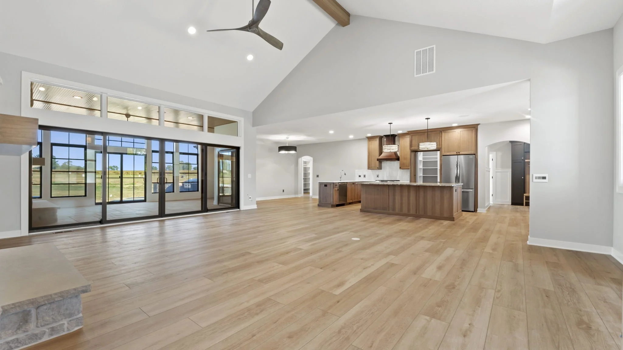 Open concept living space with large sliding glass doors leading to an outdoor area, wooden floors, modern kitchen with island and pendant lighting, ceiling fan, and white walls.