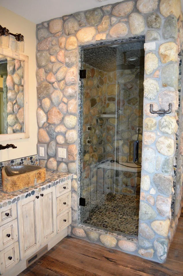 Bathroom with a rustic stone shower and a wooden vanity with a stone sink.