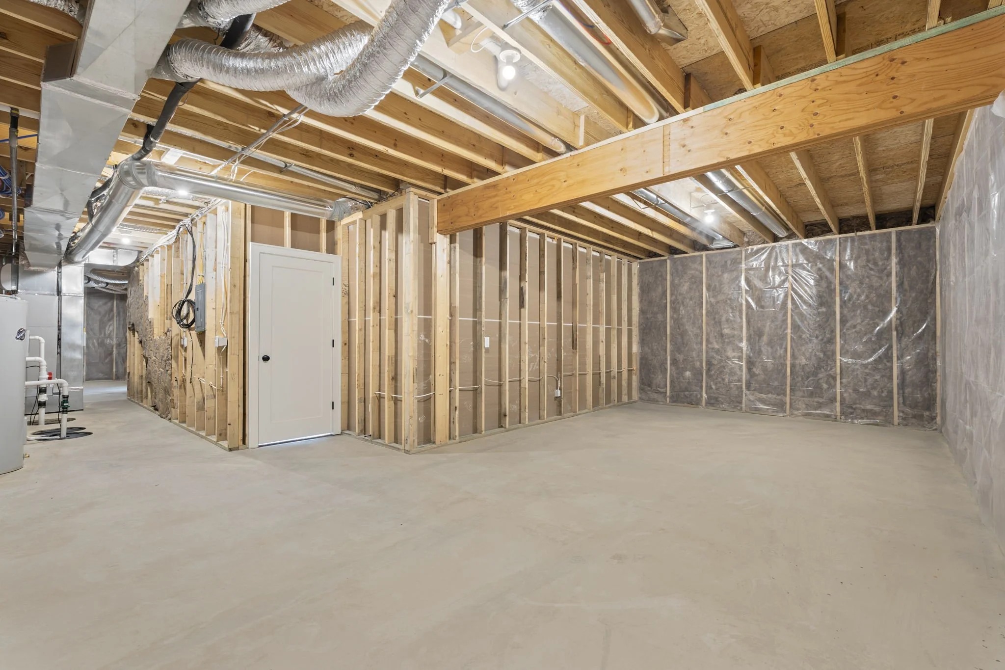 Unfinished basement with exposed wooden framing, ductwork, insulation, concrete floor, and a small white door.