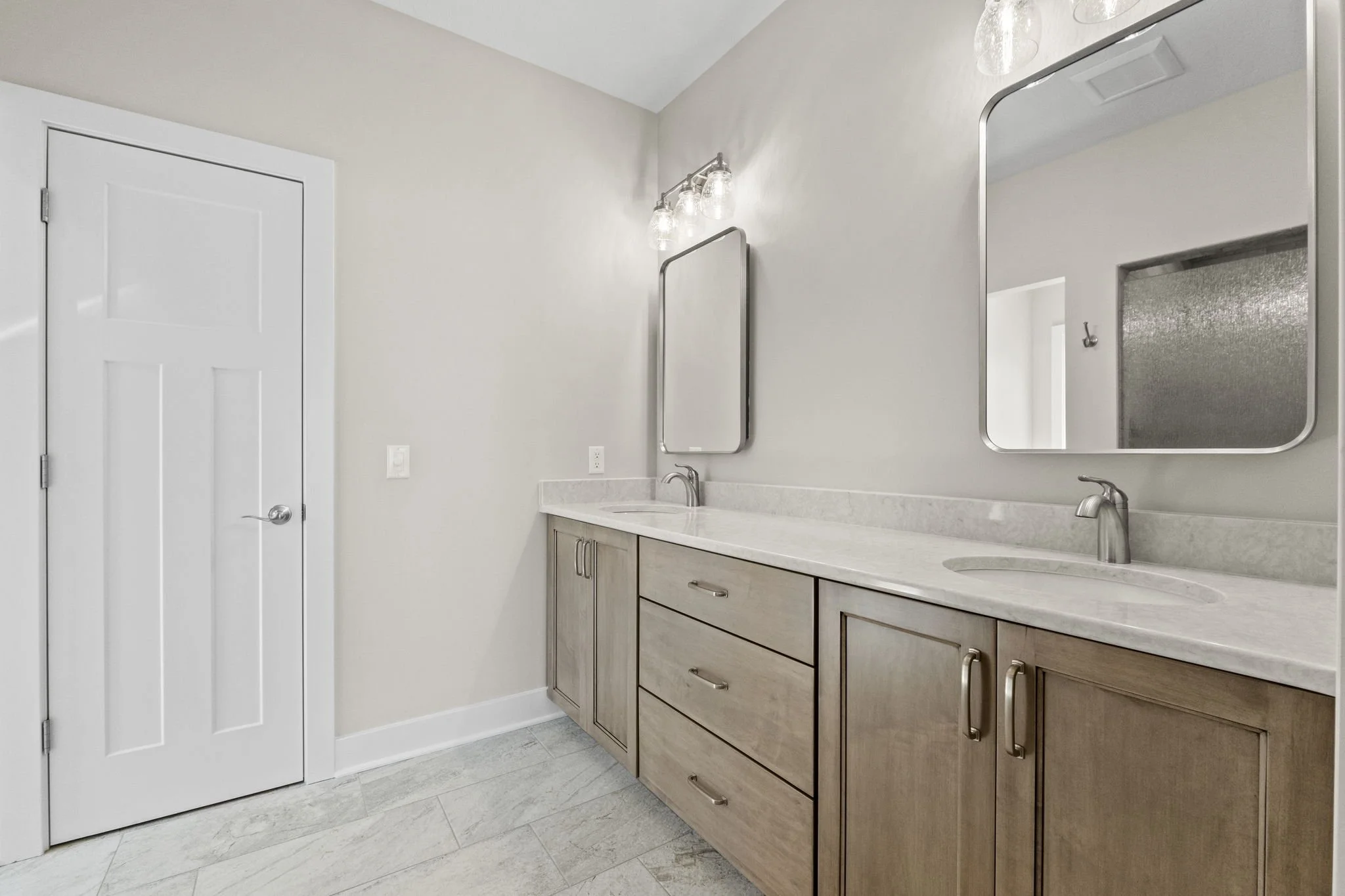 Double bathroom vanity with two mirrors, light fixtures, and two sinks in a neutral-colored bathroom.
