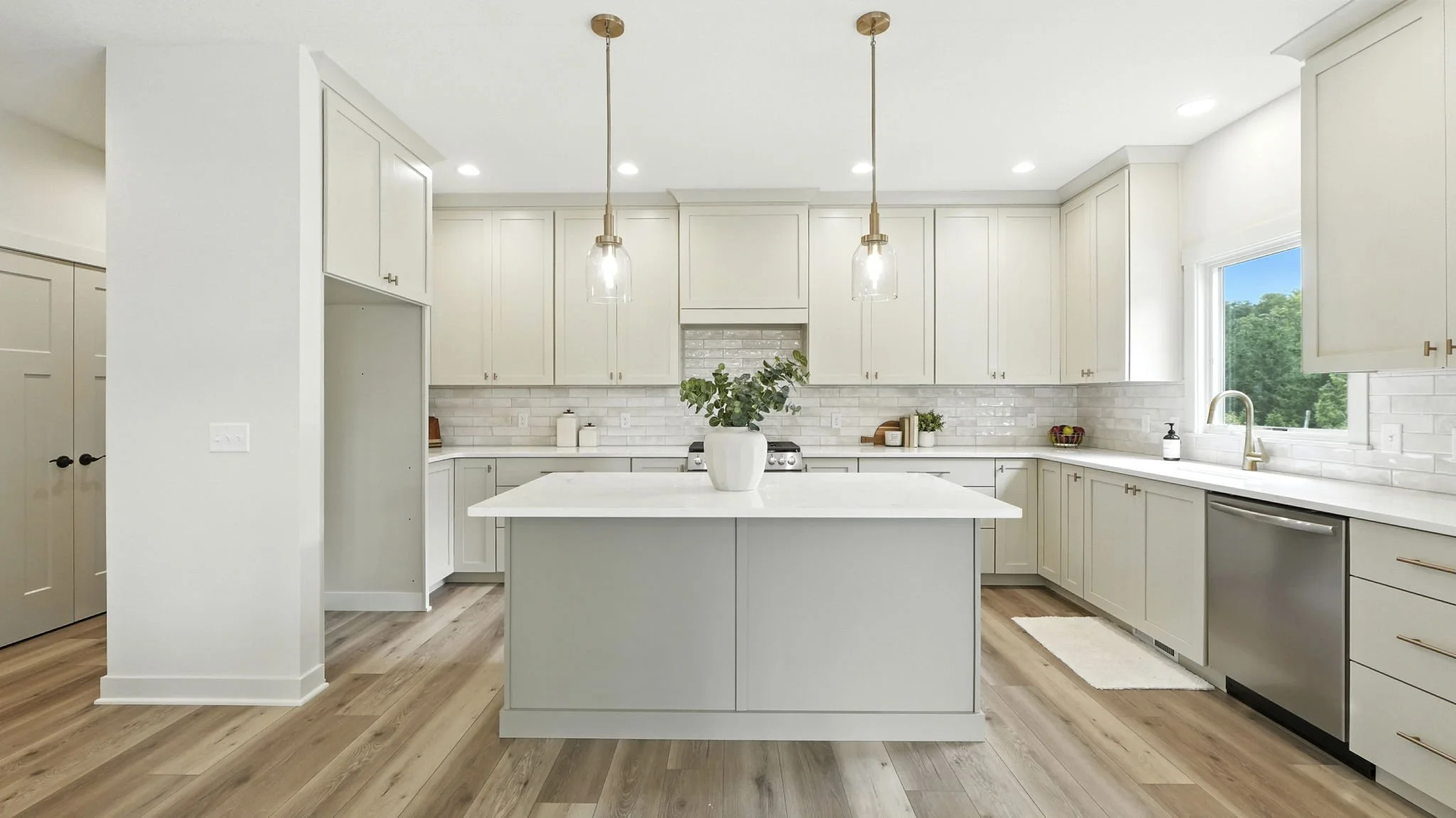 Modern kitchen with white cabinets, a large kitchen island with a potted plant, pendant lighting, a subway tile backsplash, a window above the sink, and stainless steel appliances.