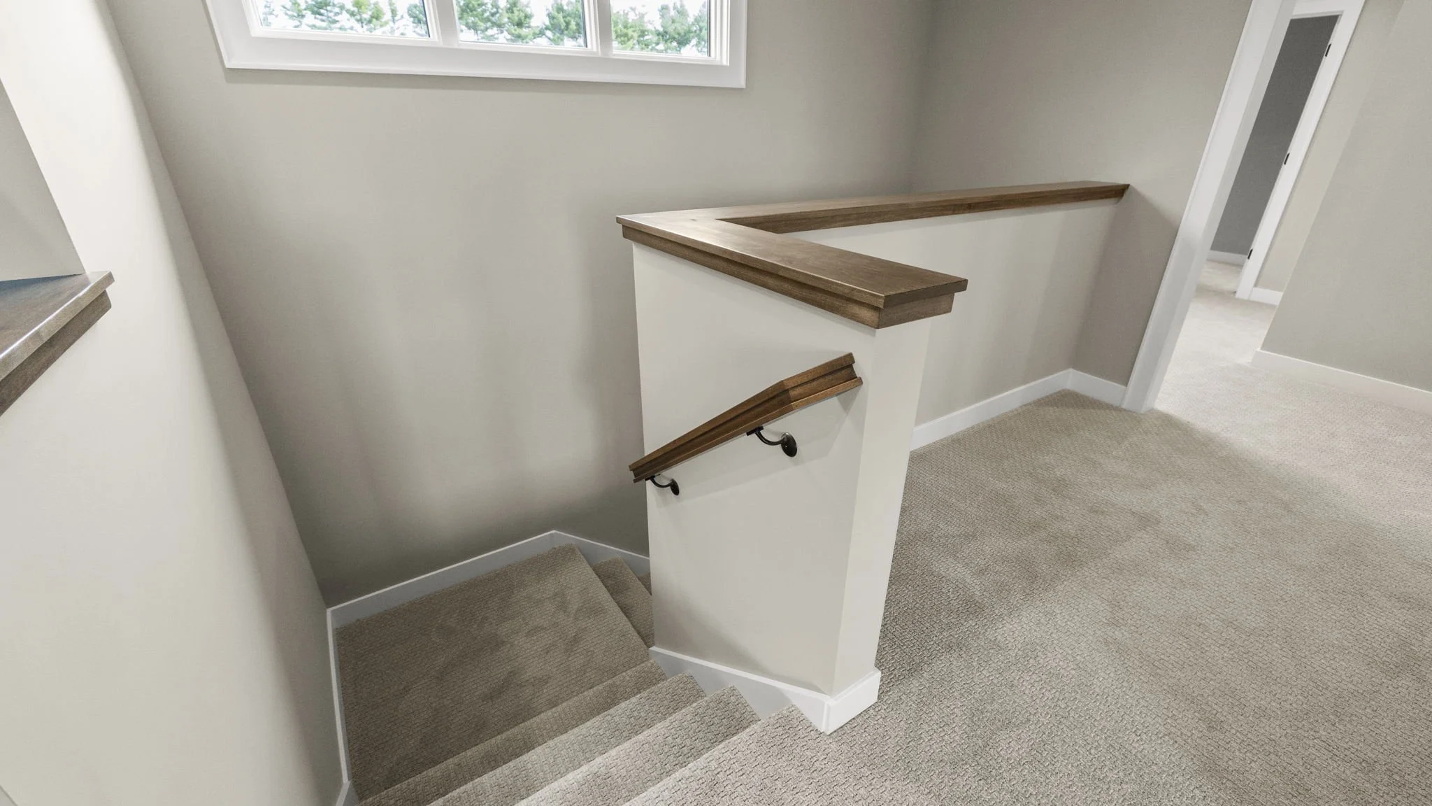 A staircase with beige carpeted steps, a white balustrade with a wooden handrail, and beige walls with white trim. There is a window at the top of the stairs, and a doorway to the right leading to a carpeted room.