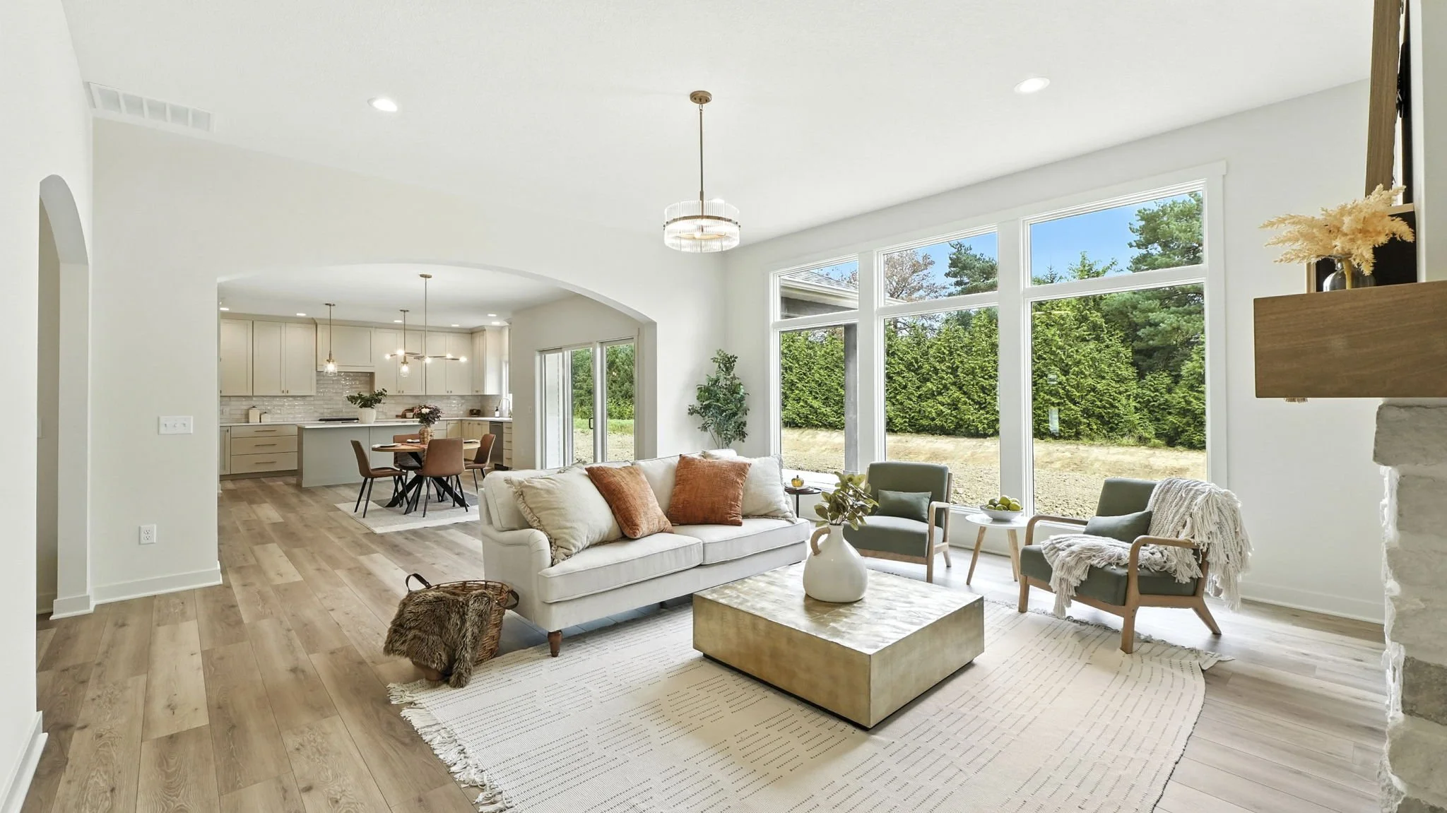 Bright living room with large windows, white walls, hardwood floors, sofa, chairs, coffee table, and view of backyard with trees