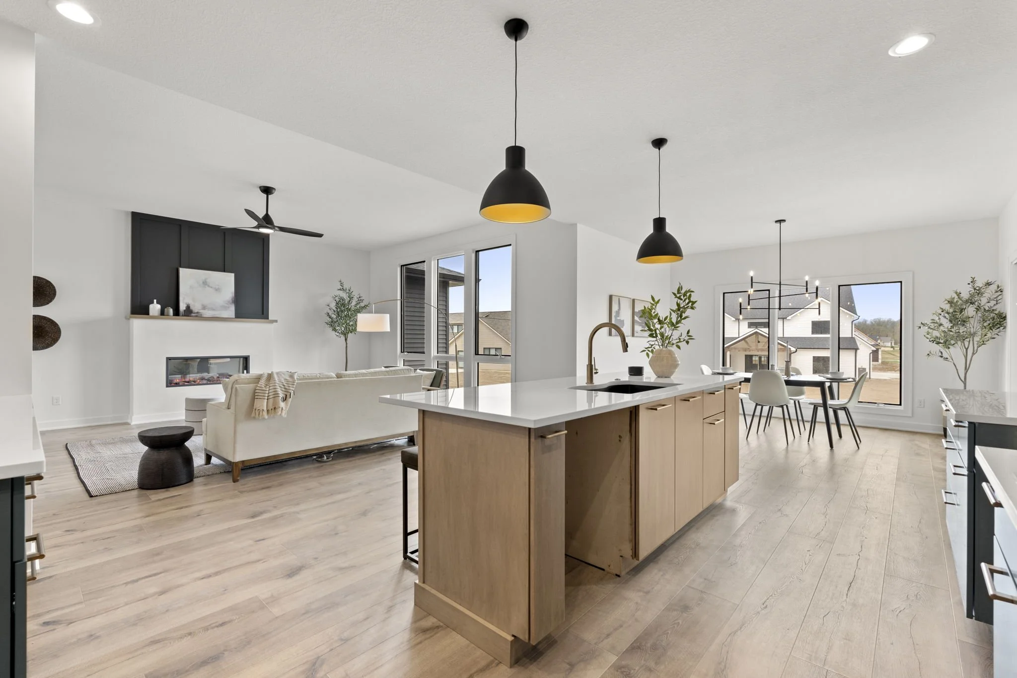 Open-concept living and dining area with a kitchen island, dining table, white sofa, fireplace, and large windows in a modern home.