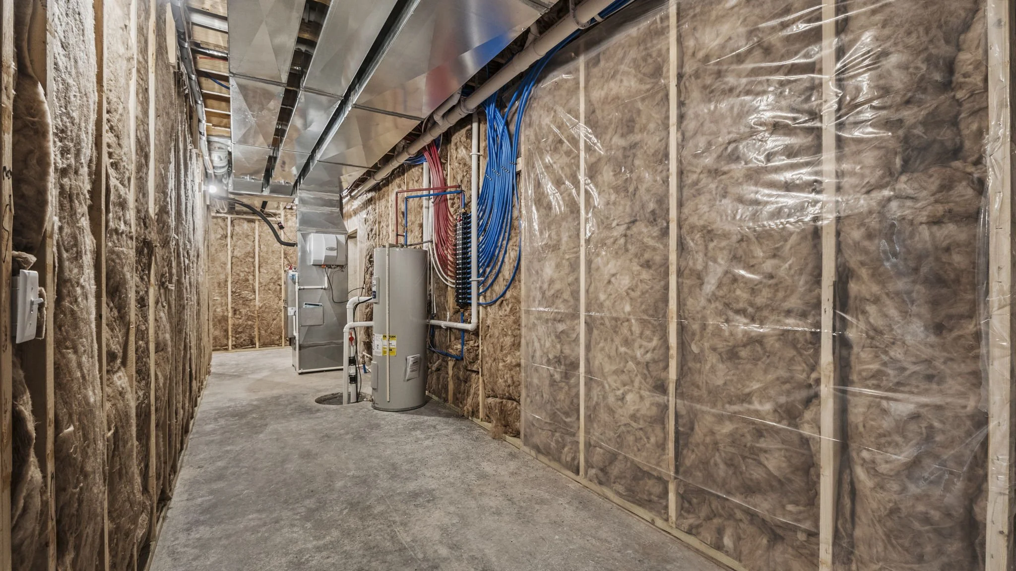 A basement with insulation on the walls, an HVAC duct system, electrical wiring, and a water heater.