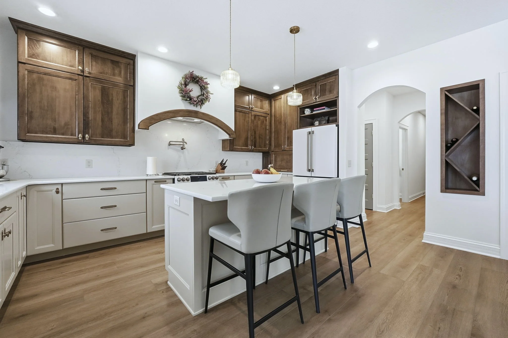 Modern kitchen with white and wooden cabinets, a white kitchen island with chairs, pendant lights, and decorative wreath on the wall.