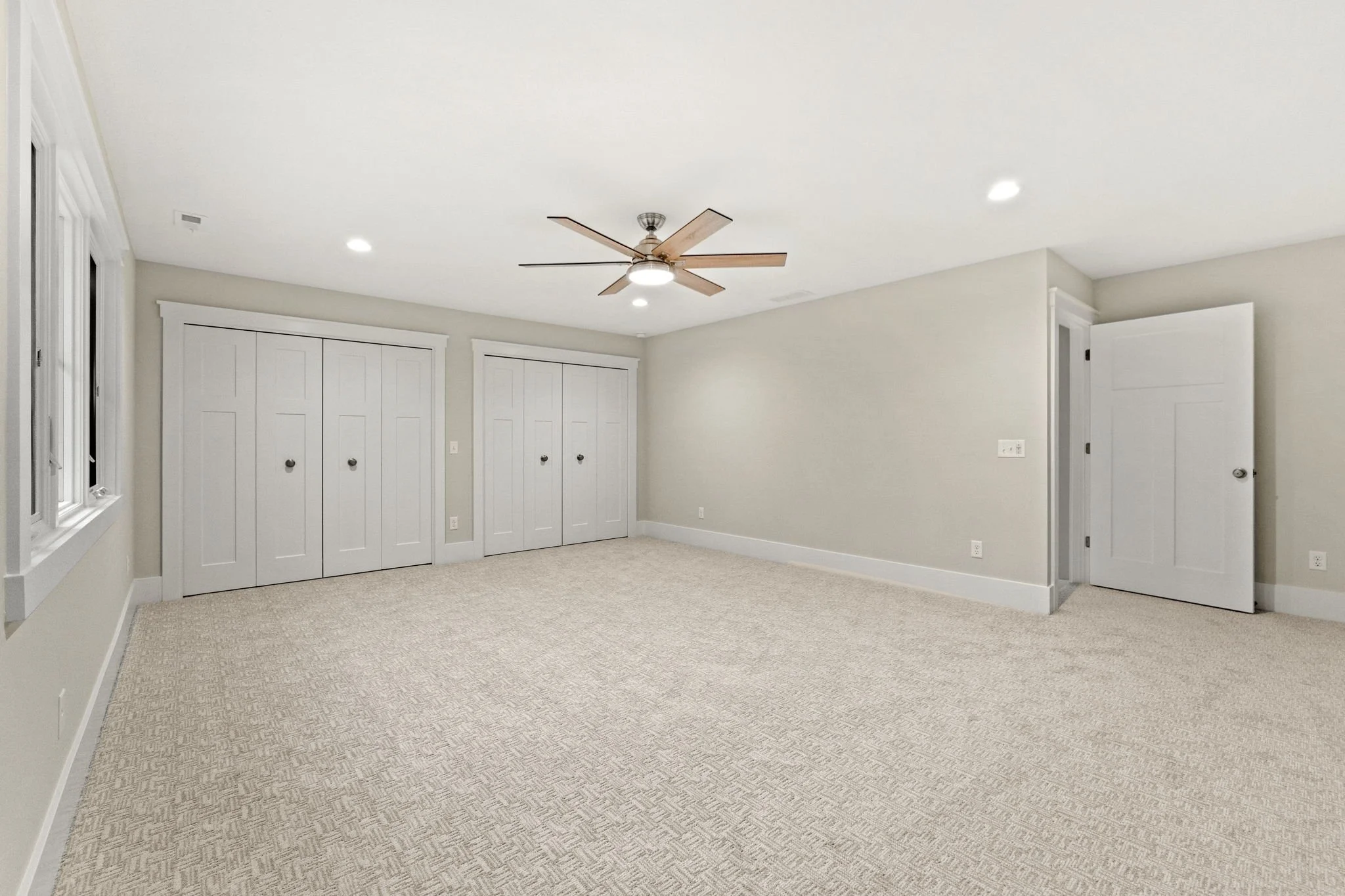 Empty bedroom with beige carpet, white walls, white doors, a window, and ceiling fan with wooden blades.