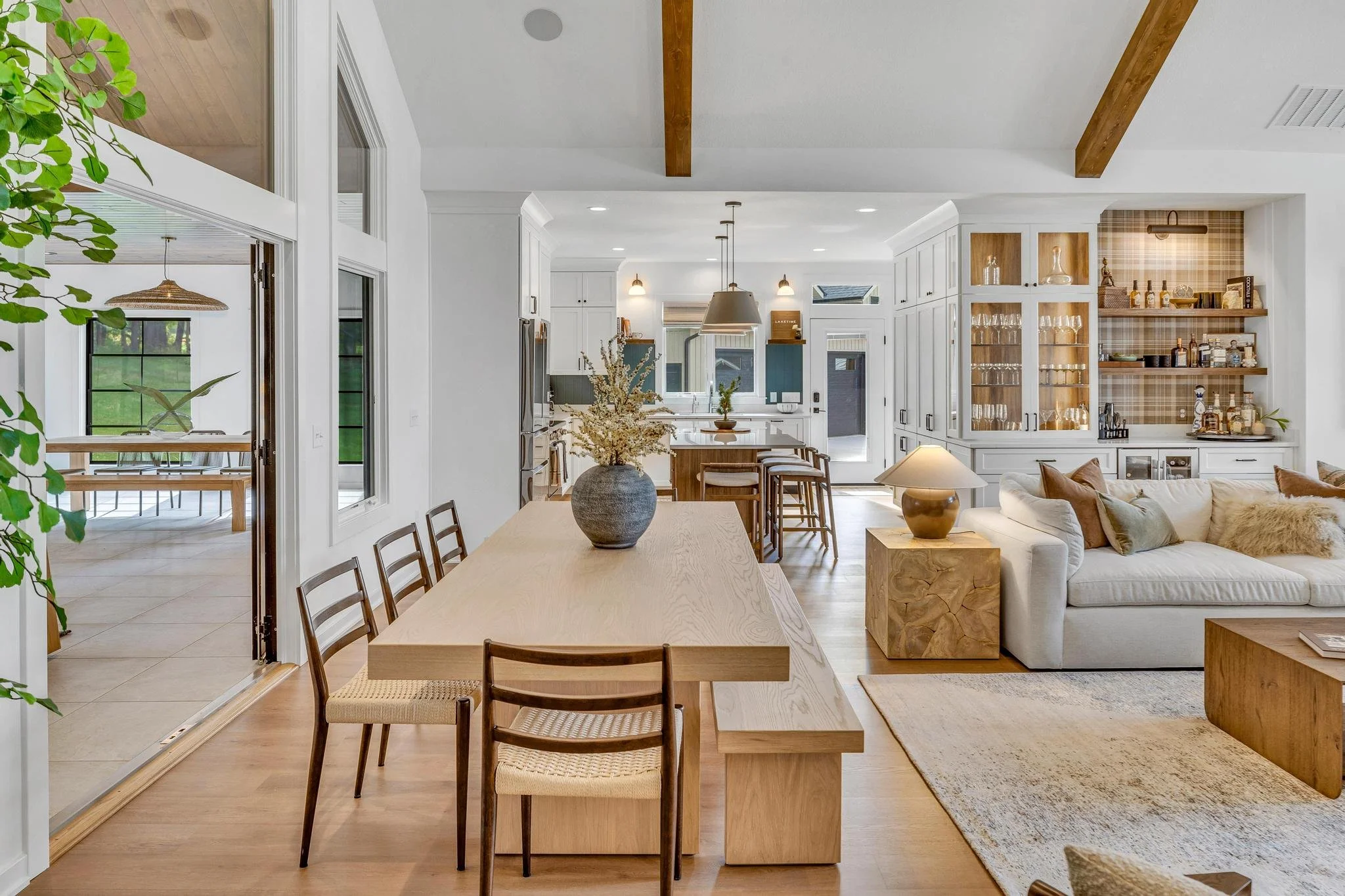 Open concept living room and kitchen with white cabinets, a large dining table, and a cream sofa, decorated with neutral tones and wooden accents.