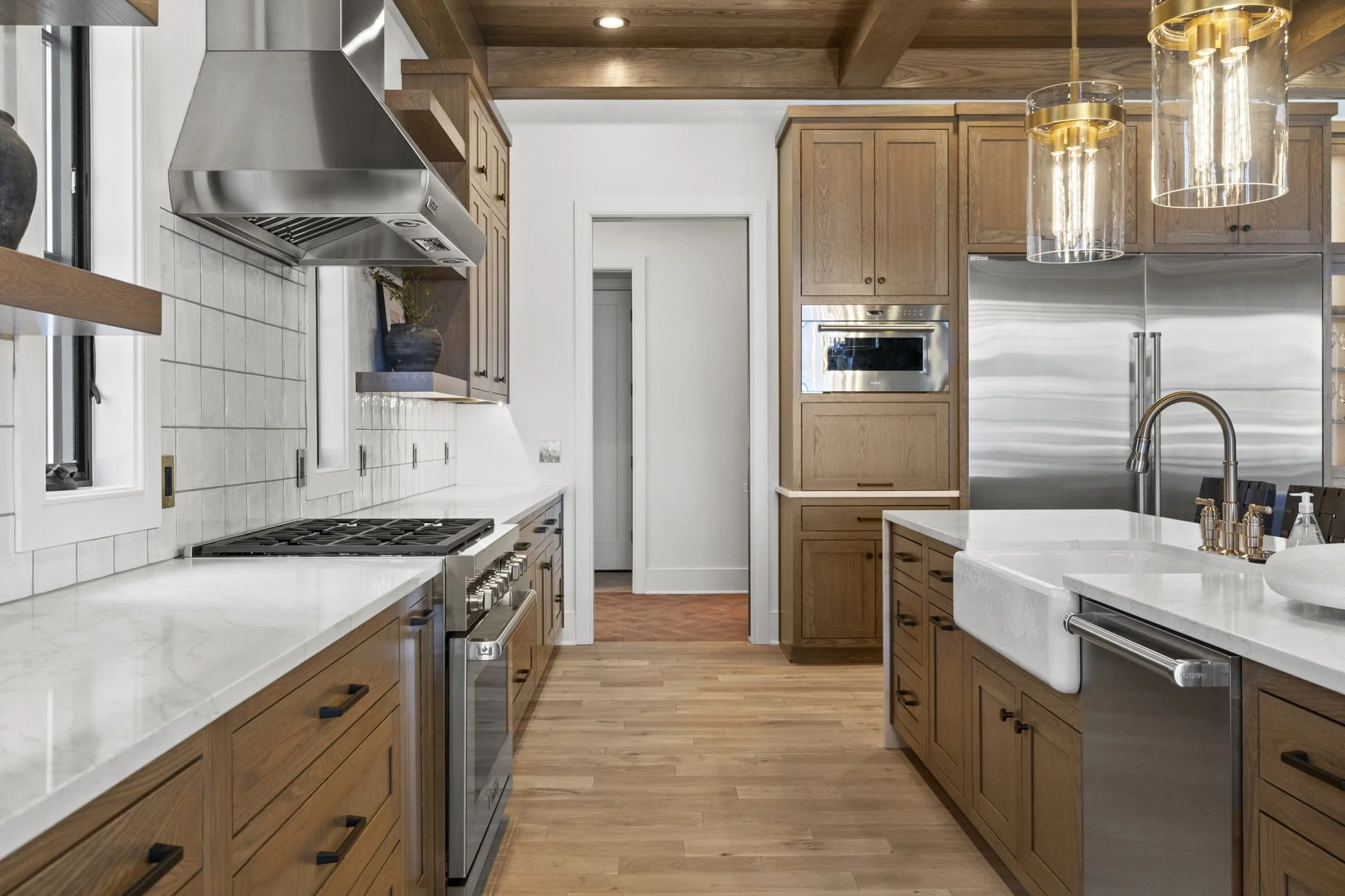 Modern kitchen with wooden cabinets, white marble countertops, stainless steel appliances, pendant lights, and a farmhouse sink.