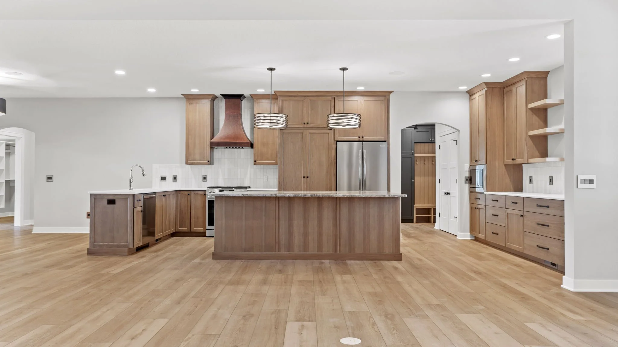 Modern kitchen with wooden cabinets, a large island with a granite countertop, stainless steel refrigerator, and pendant lighting