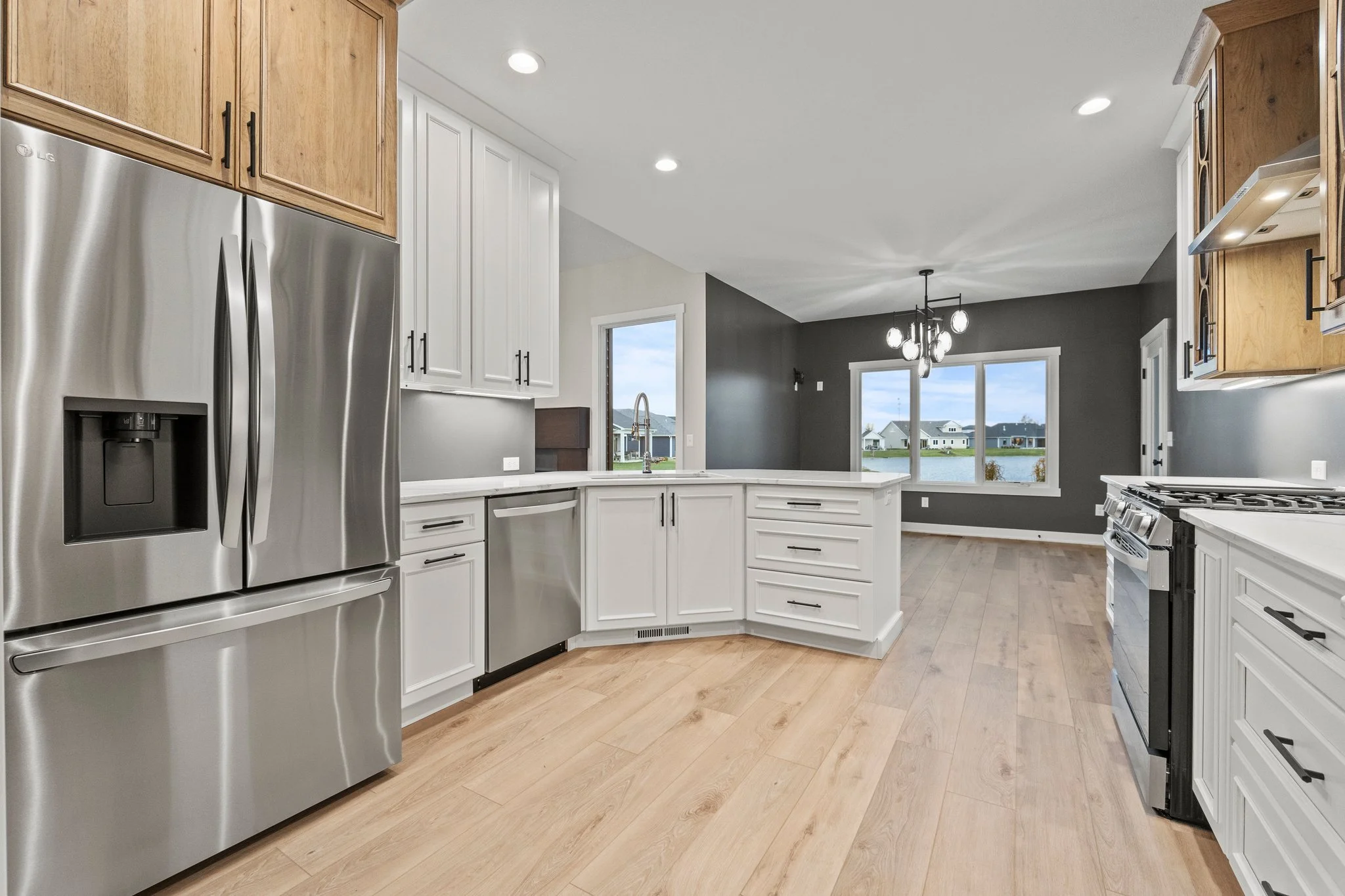 Modern kitchen with white cabinets, stainless steel appliances, wooden accents, and a view of a lake through large windows.
