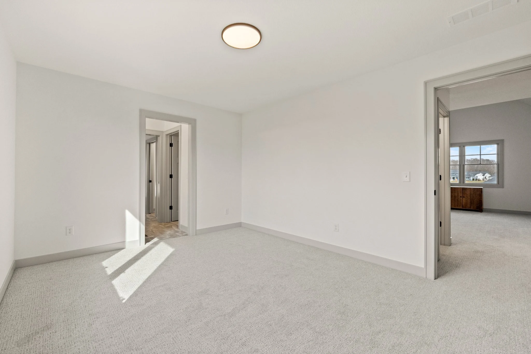 Empty white room with carpeted floor, multiple doorways, and a window showing a view of neighboring houses.