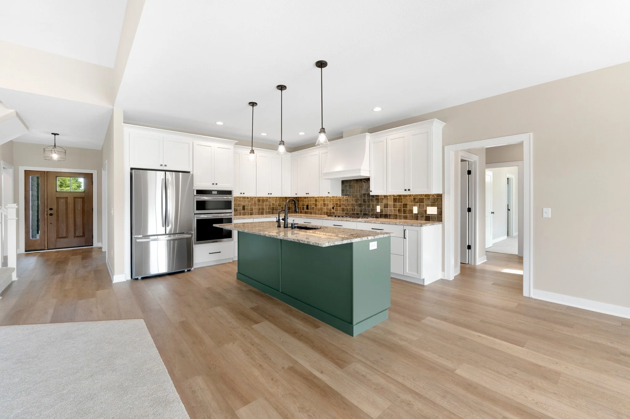 Modern kitchen with white cabinets, a green island, wooden flooring, stainless steel appliances, and pendant lighting.