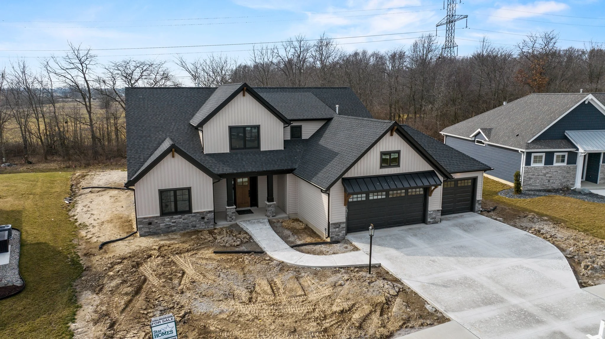 Newly constructed two-story house with attached garage, front yard, and a sidewalk, in a neighborhood with other houses and trees in the background.