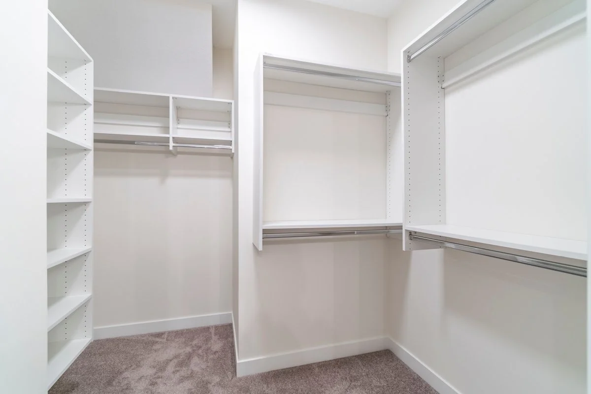 empty walk-in closet with white shelves and hanging rods, beige carpeted floor.