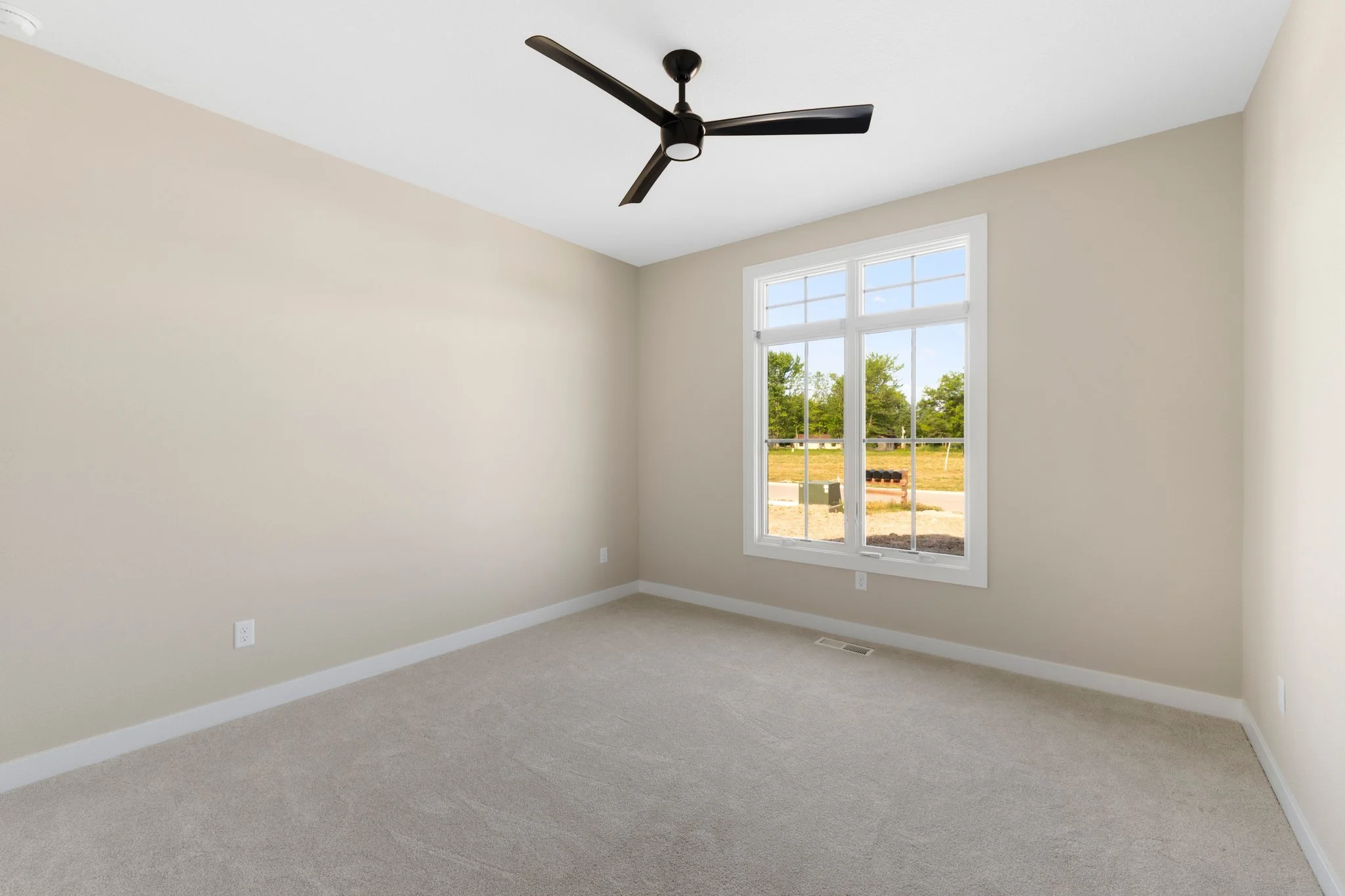 Empty room with beige walls, a large window, carpeted floor, and a black ceiling fan.