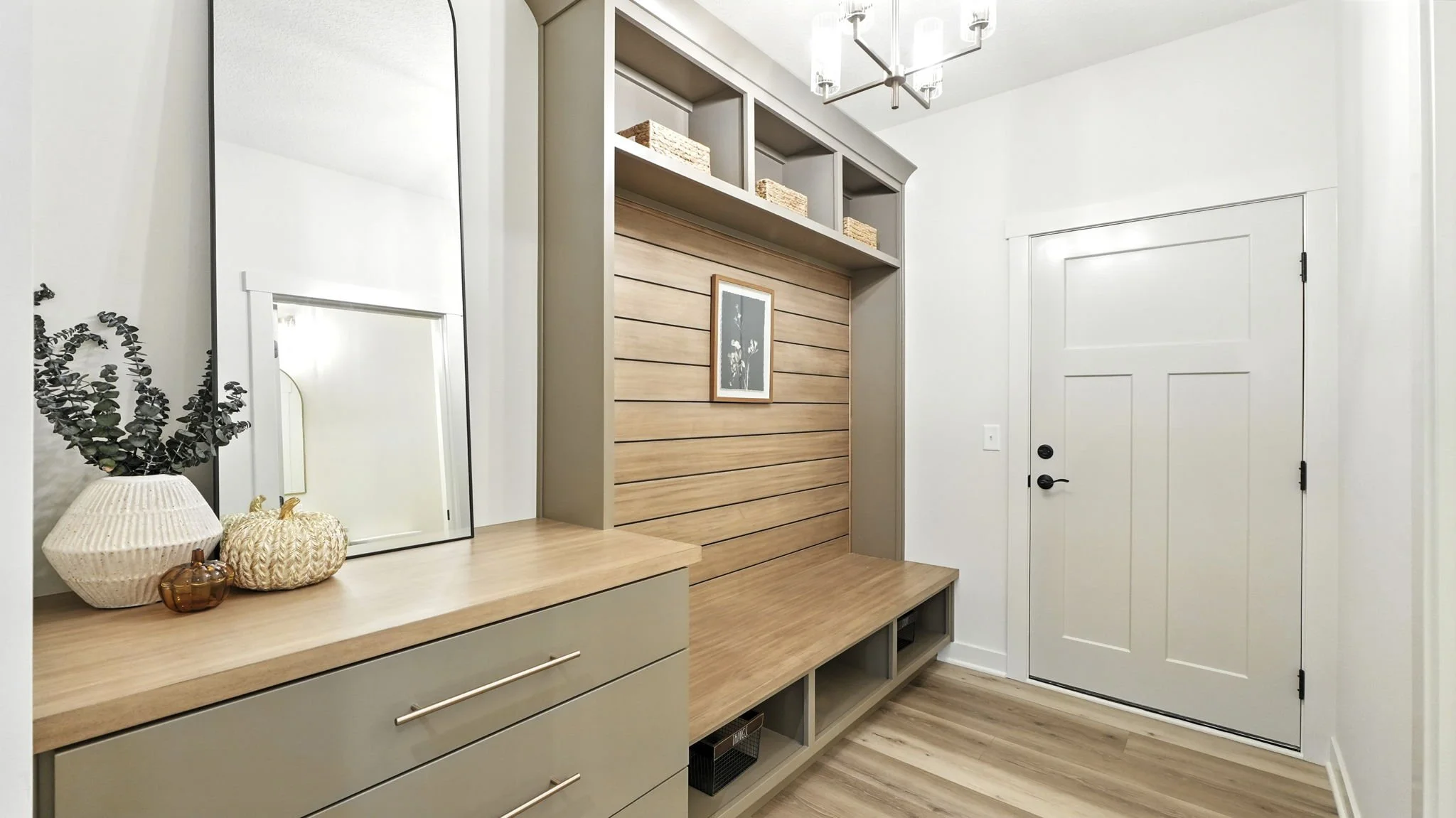 Entryway with beige and wood finishes, white walls, a built-in bench with open cubbies, a decorative wall with horizontal wood paneling, a framed floral artwork, and a small closet door.