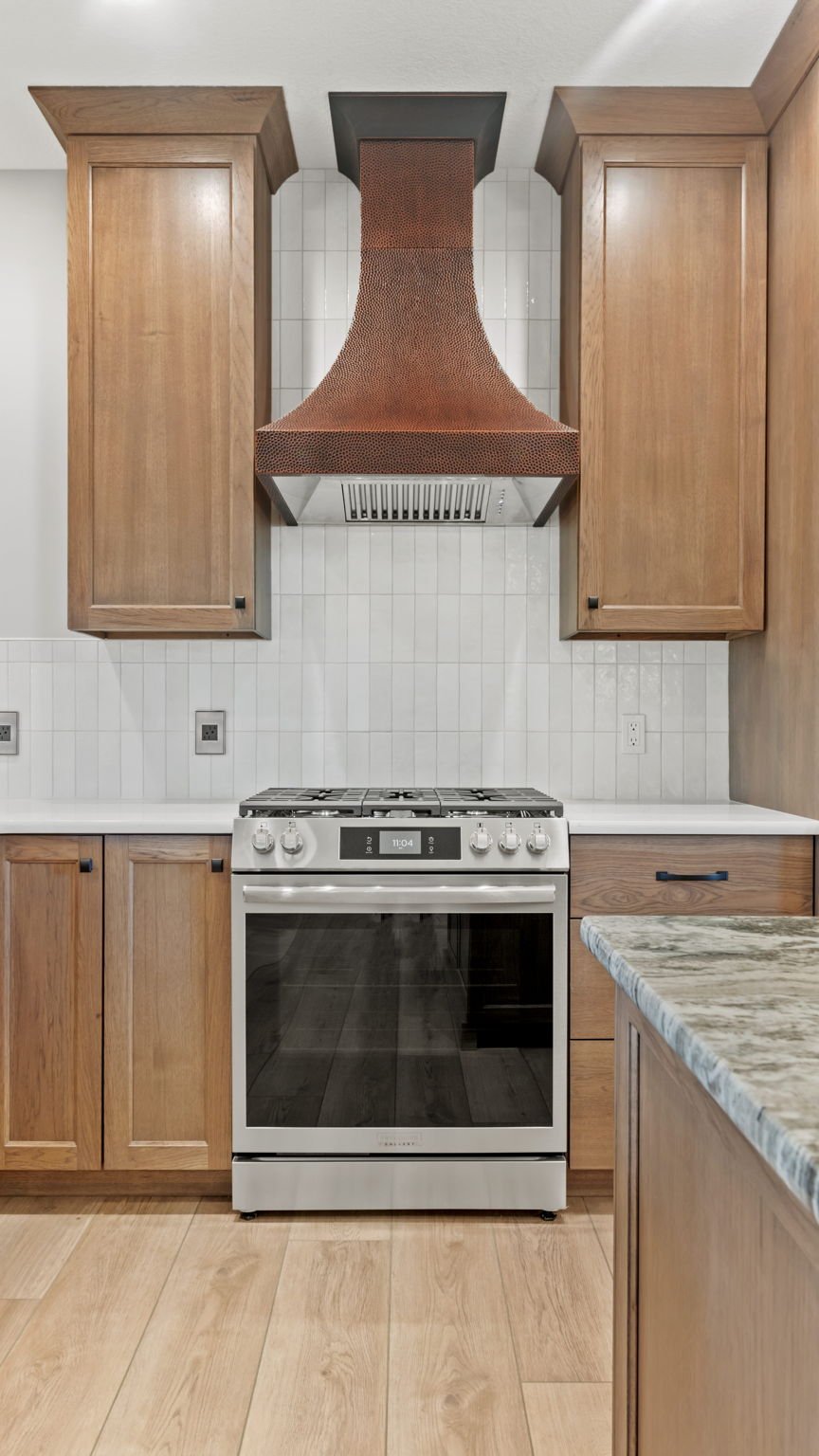 A kitchen with wooden cabinets, a stainless steel oven, and a distinctive copper-colored ventilation hood above the stove.
