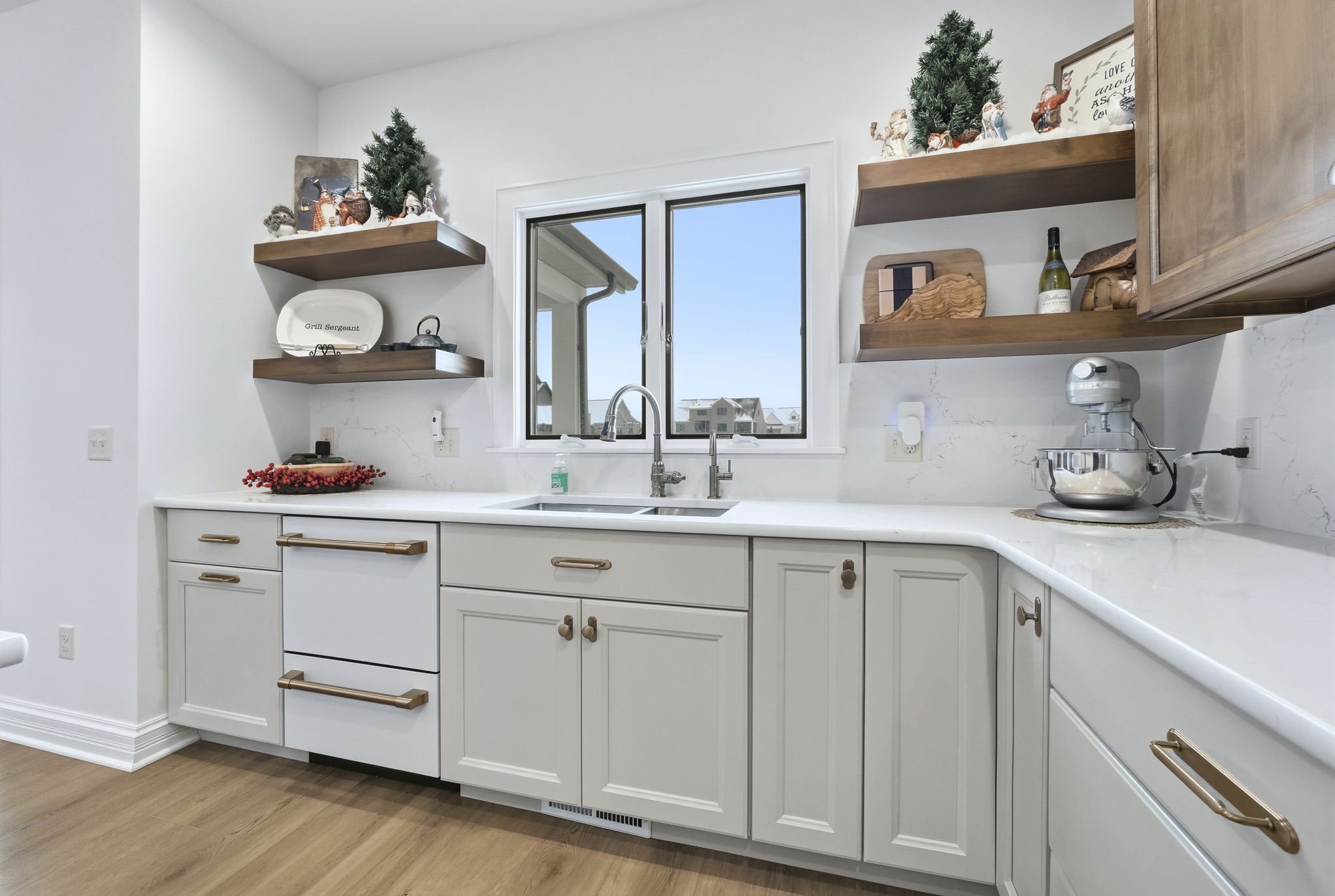 White kitchen with wooden open shelves, a window above the sink, and decorative items including small Christmas trees and figurines on the shelves.