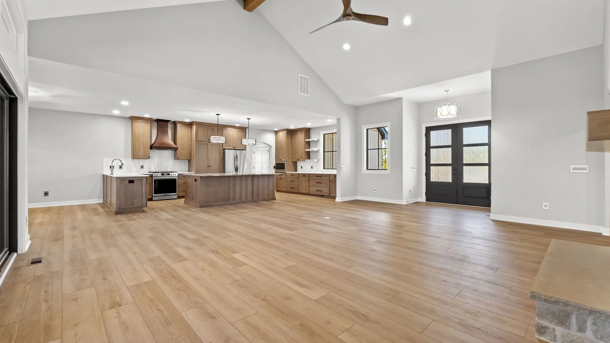 Spacious open-concept living area with wood flooring, modern kitchen with island, stainless steel appliances, and pendant lighting, entryway with double doors, and large windows for natural light.