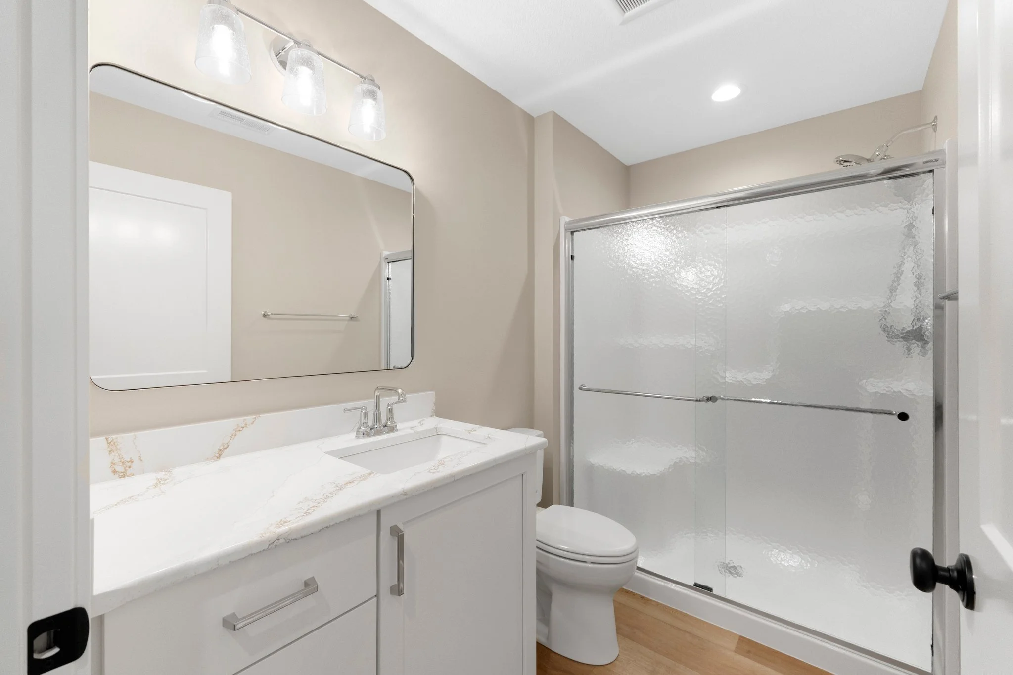 Modern bathroom with a white vanity, marble countertop, mirror, and frosted glass shower with a sliding door.