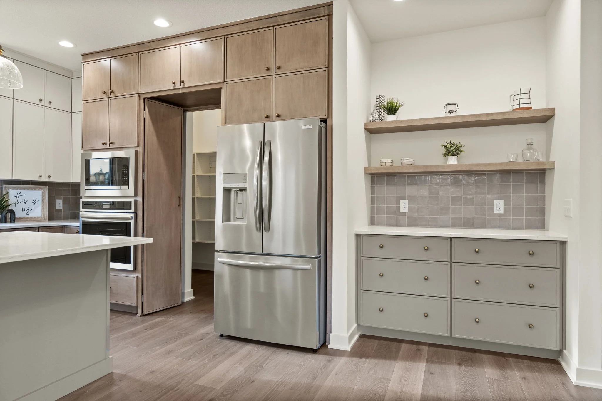 Modern kitchen with a stainless steel fridge, wooden cabinets, and open floating shelves with decorative items.