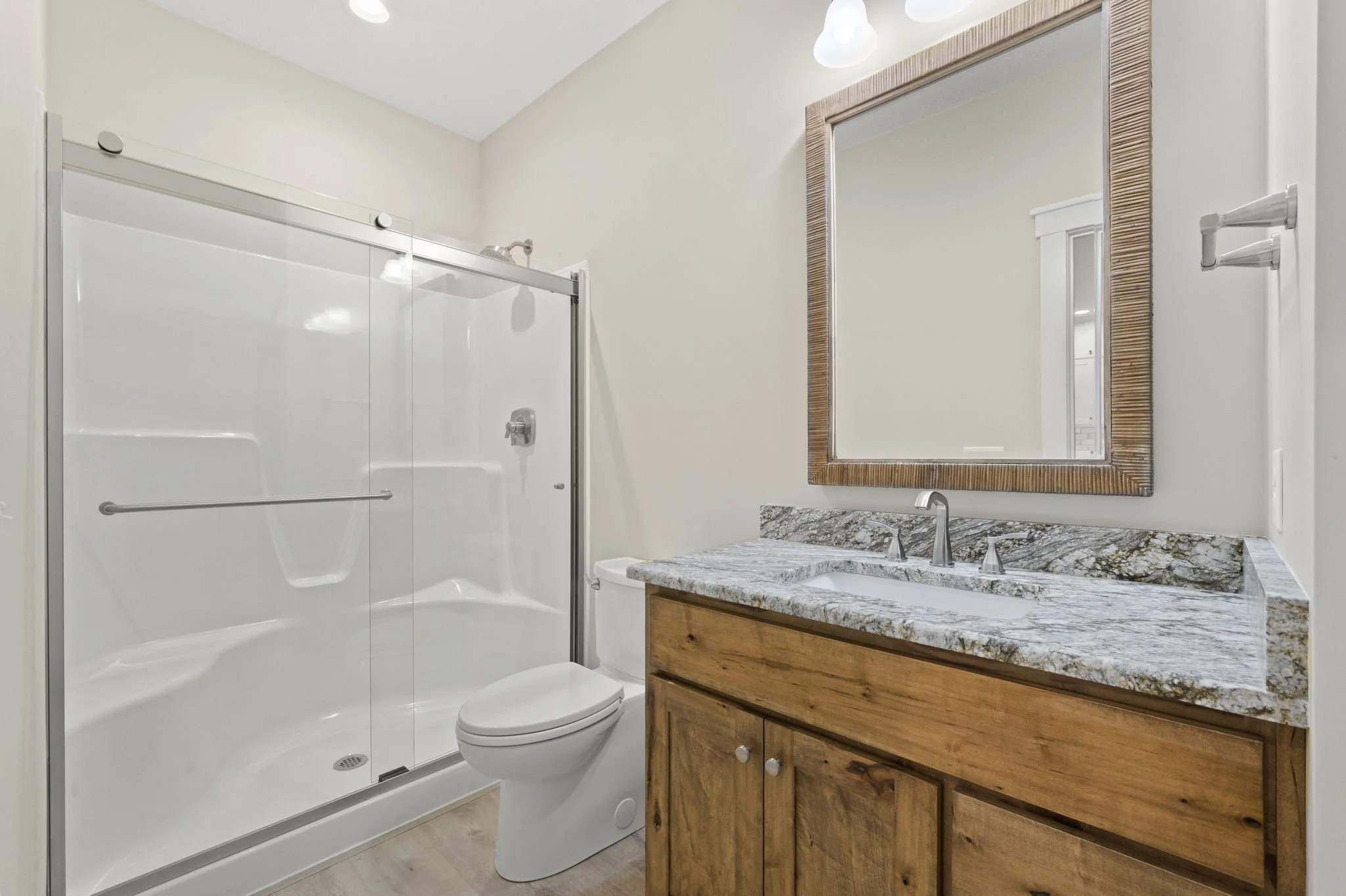Bathroom with a glass-enclosed shower, a white toilet, a wooden vanity with a granite countertop, and a mirror above the sink.